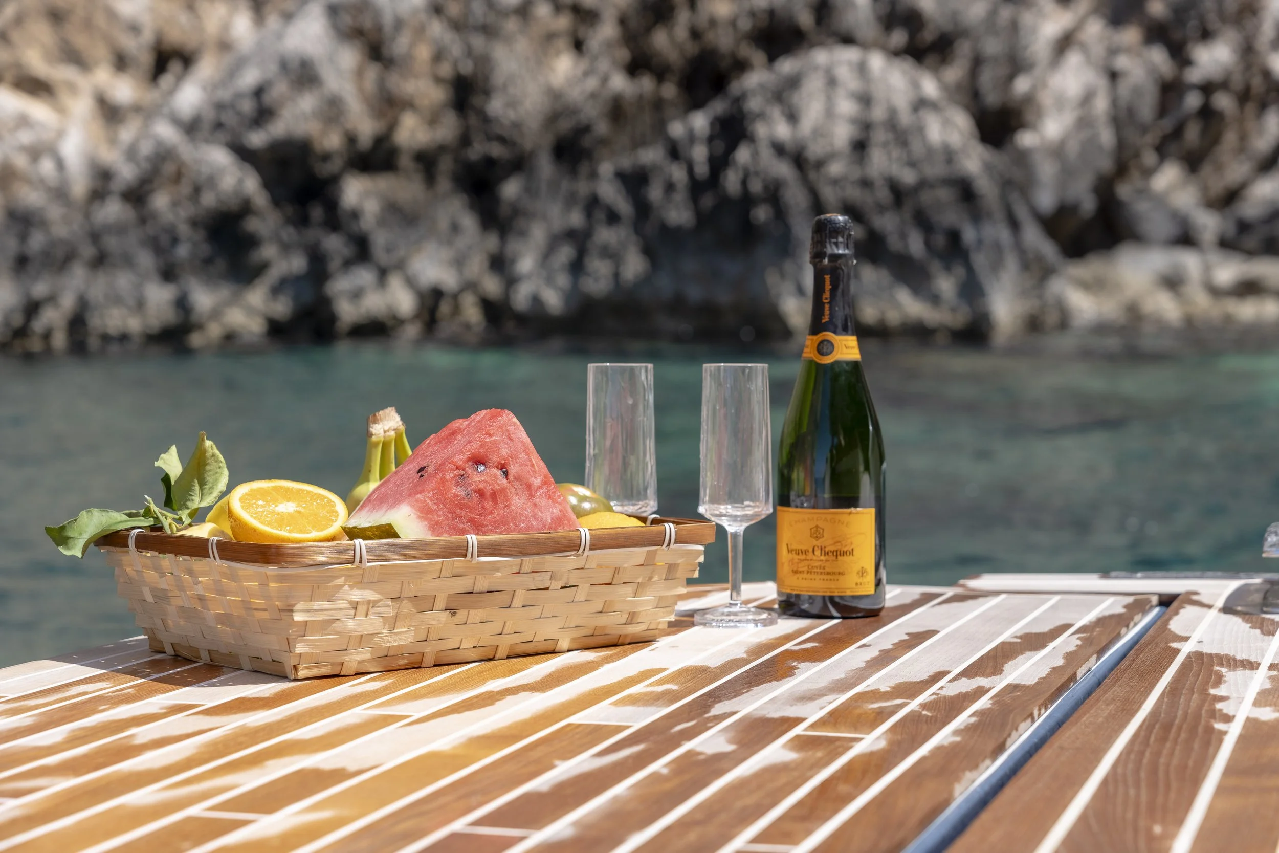 Fresh fruit and champagne set on the bow of a boat with bright blue Mediterranean Sea in the background