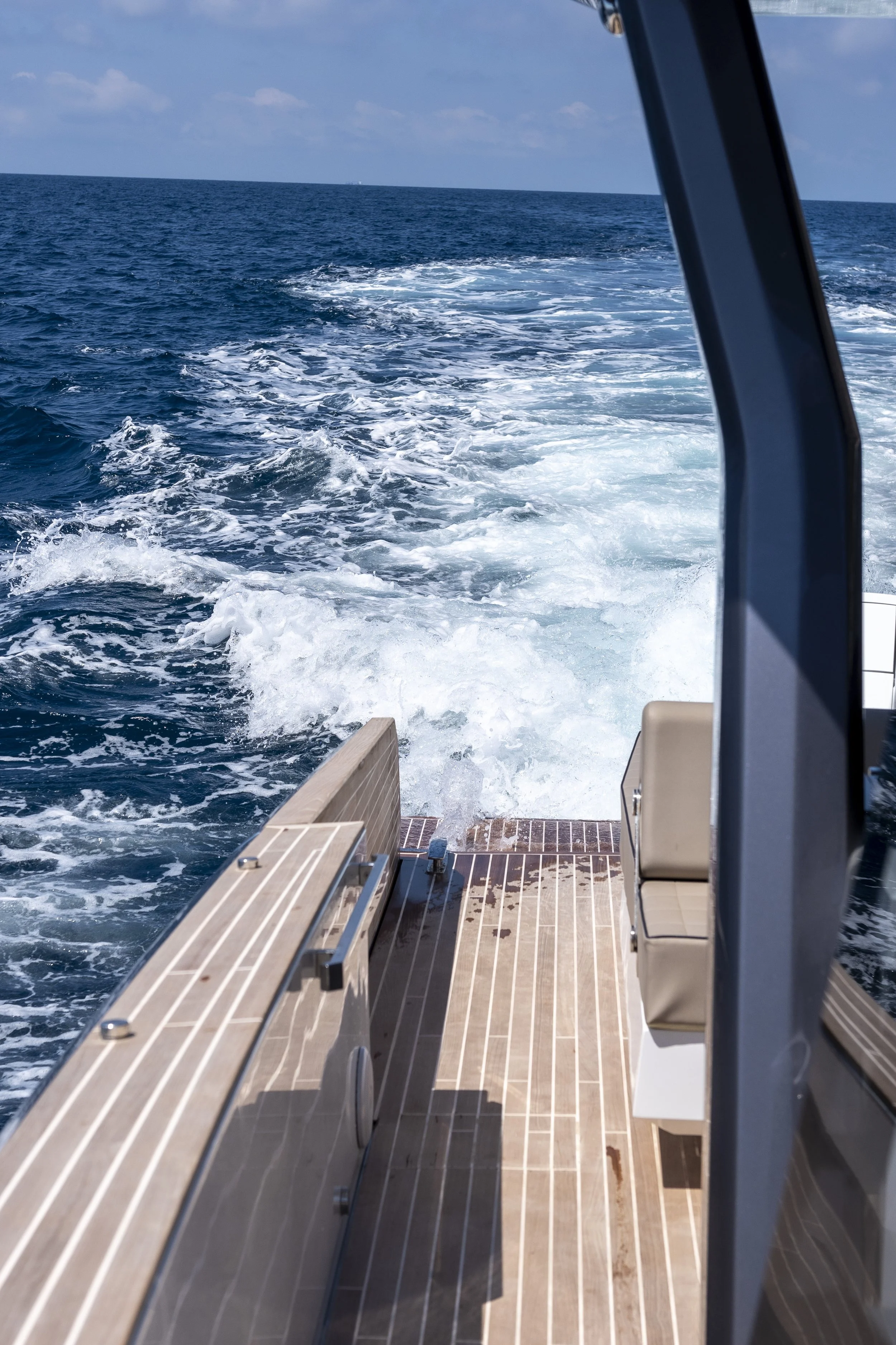 View from the back of a boat showing blue ocean water and a clear sky, with wake created by the boat.