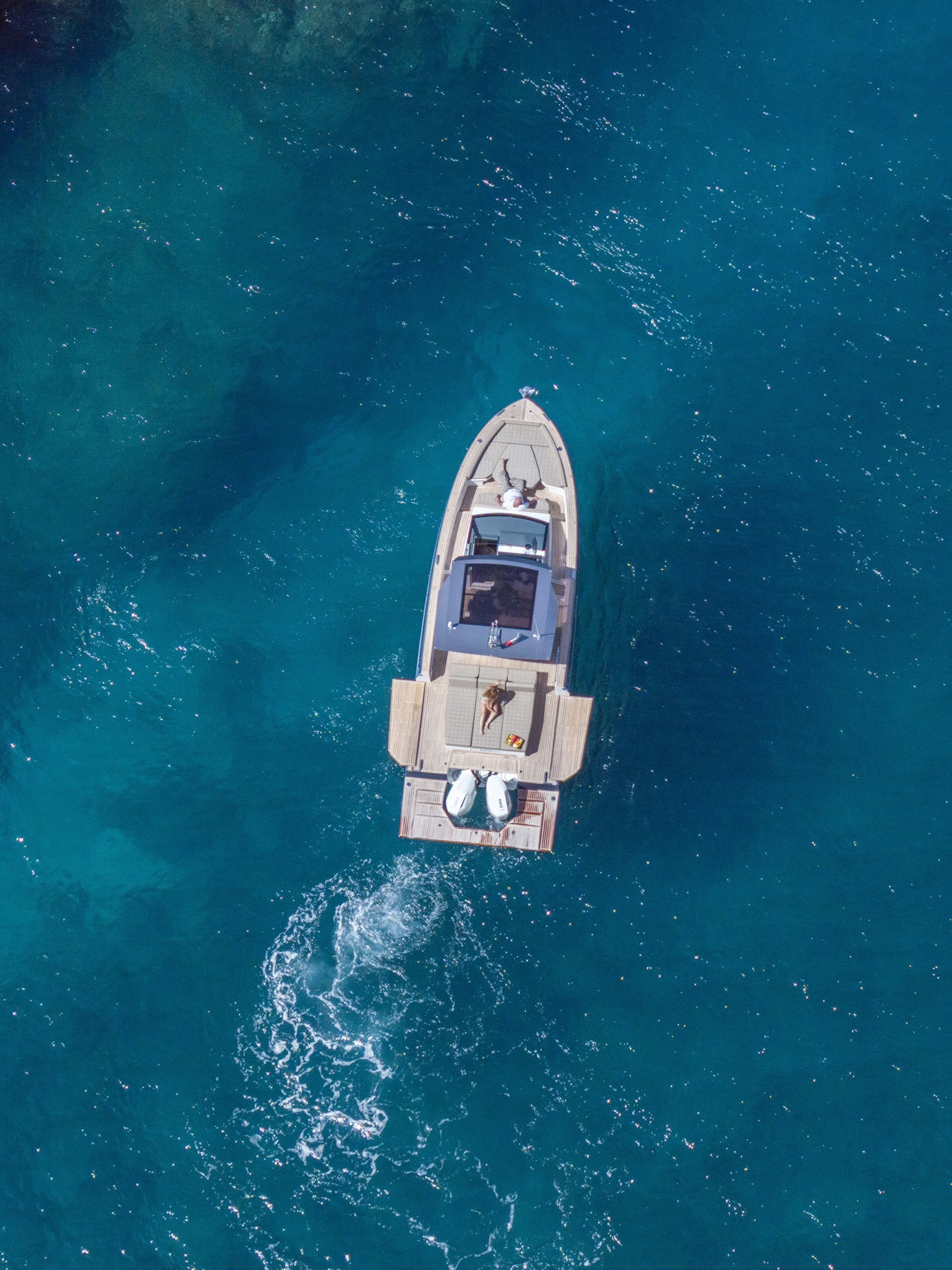 Aerial view of a boat with people on board sailing on blue water.