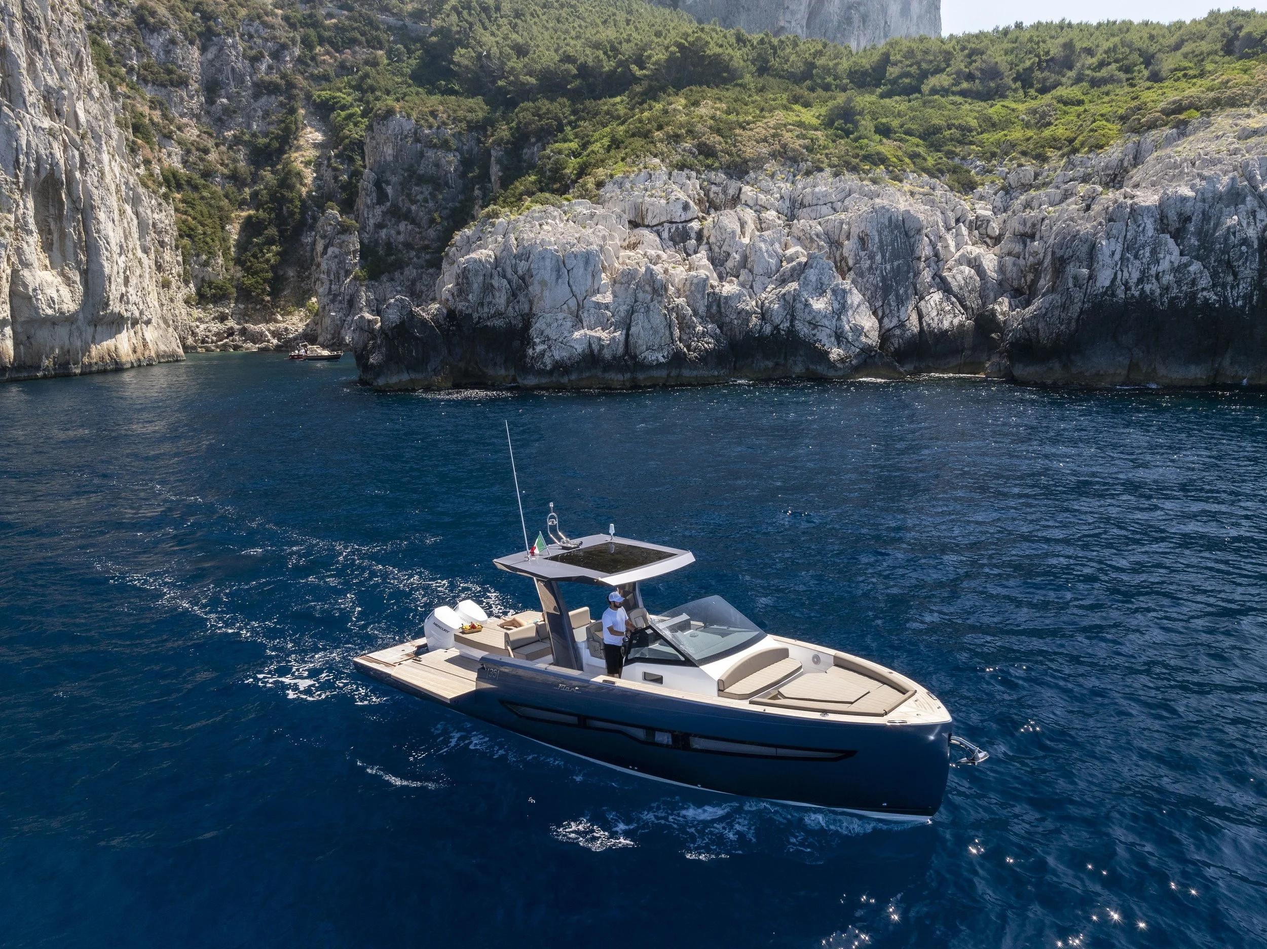 A luxury boat sailing in deep blue water, near rocky cliffs and green hills.