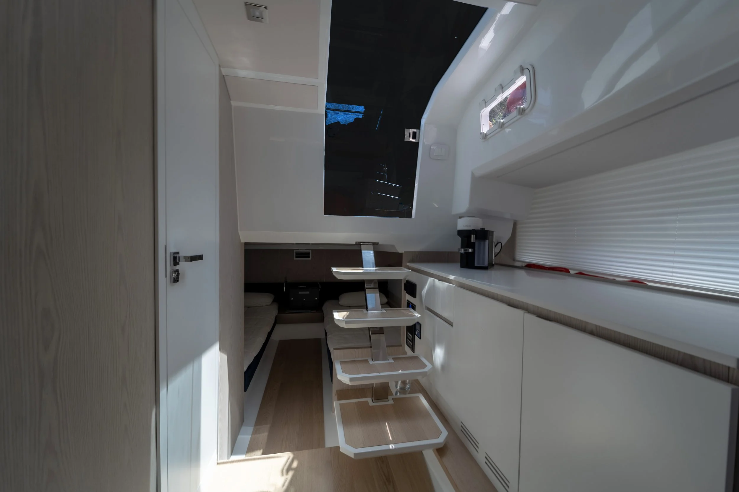 Interior of a yacht cabin with a small table, seating, a television, a coffee maker, and window blinds.