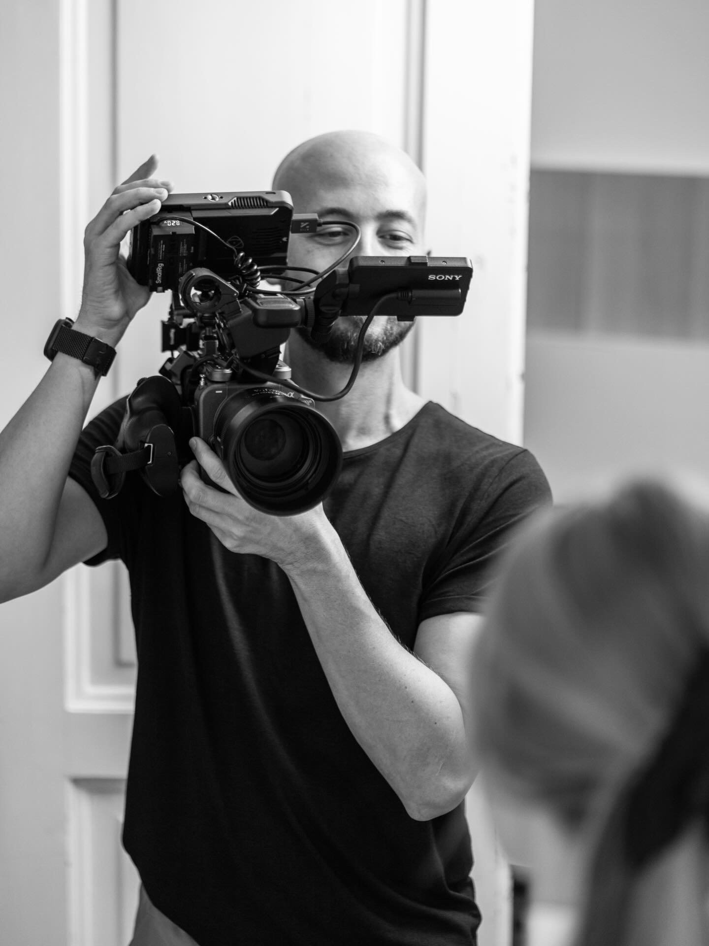 A man with a bald head filming with a professional video camera.