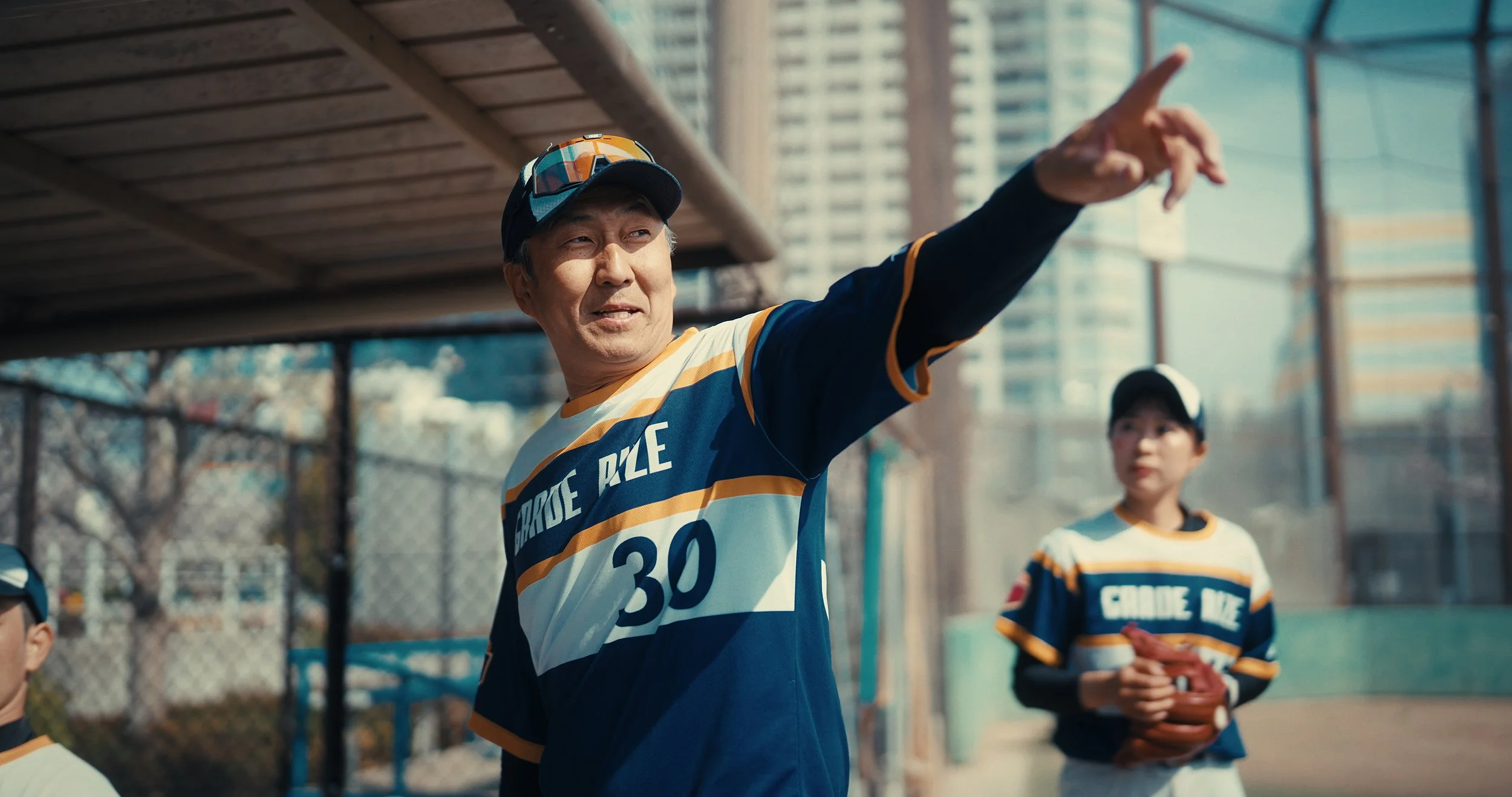 Young woman with colorful hair, choker necklace, and tattoo, lying on a bed with neon sign and illuminated WhatsApp icon reflected in the mirror, holding a book and looking at the camera.
