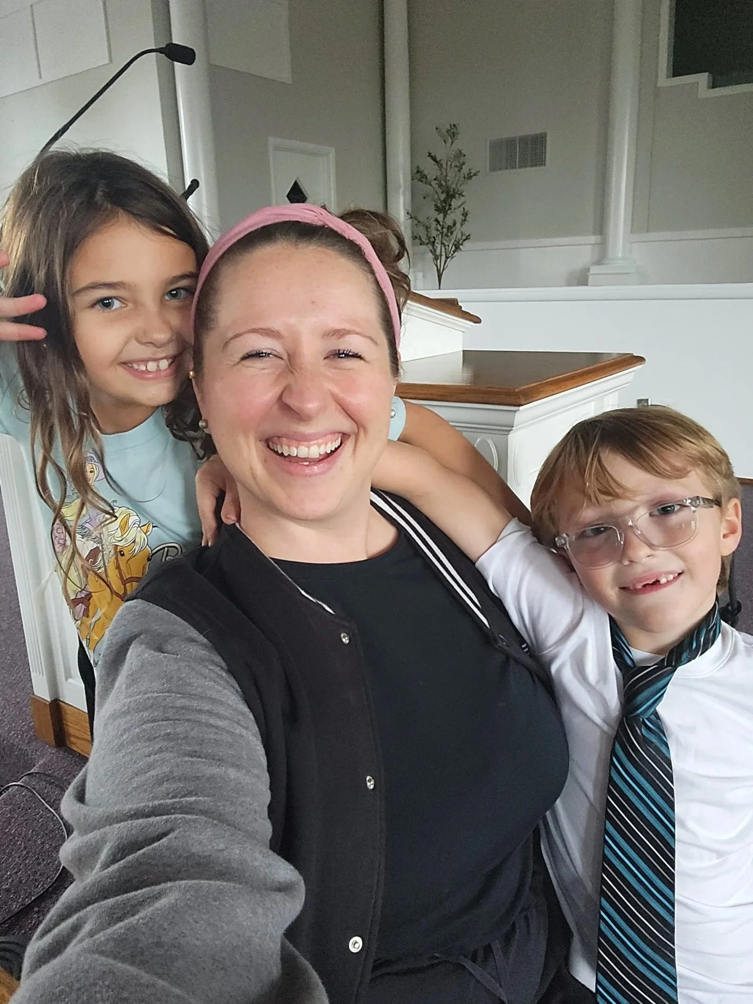A young, adult woman is posing for a picture with her students around her. Everyone is smiling. The background looks like a church.