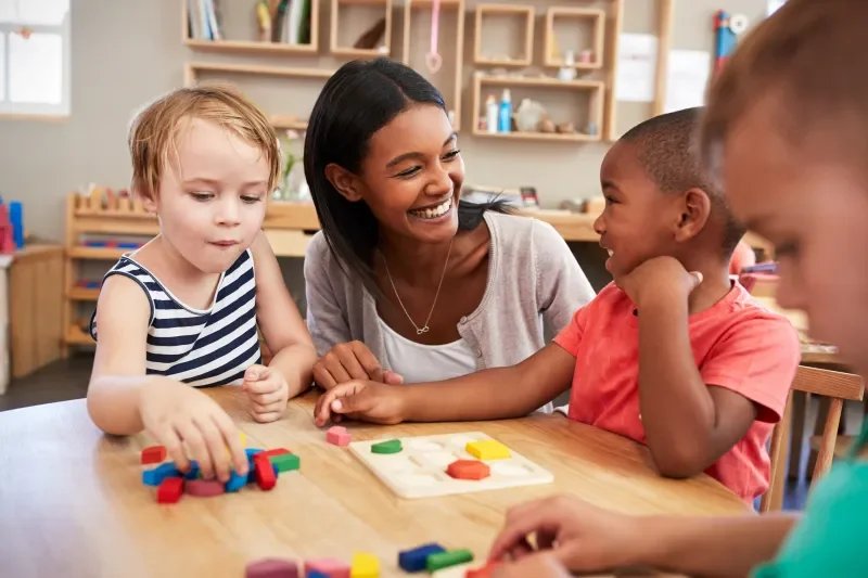 A happy teacher smiles at another student while they work on shapes in a small group learning environment at a hybrid microschool in Nashville.