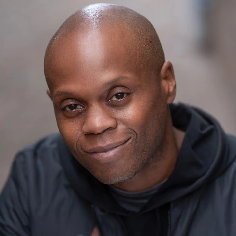 Gavin Gordon headshot.  A man with a shaved head and a slight smile, wearing a dark jacket.
