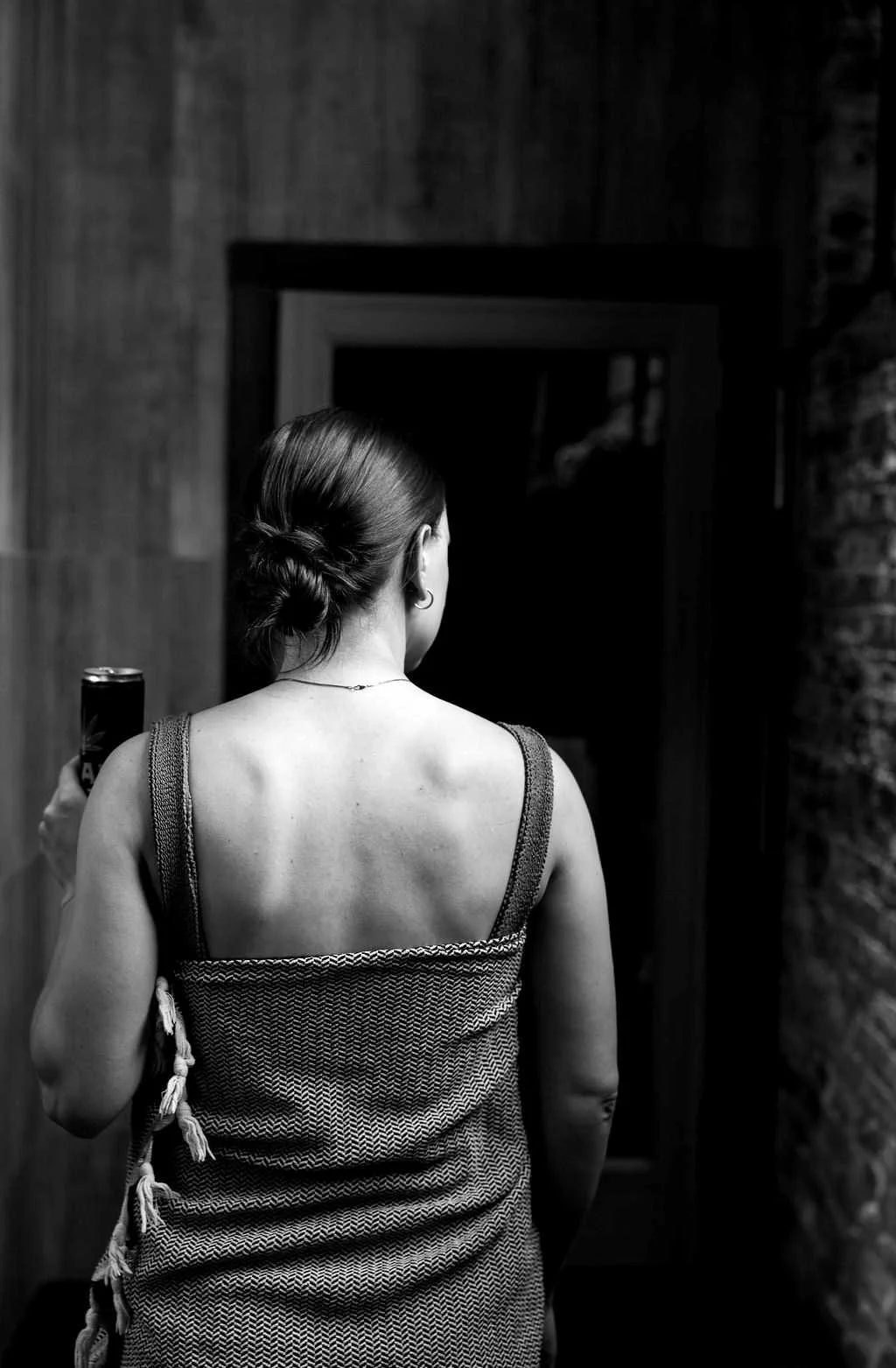 Back view of a woman with her hair in a bun, wearing swimsuit and Turkish towel, in front of the sauna door.