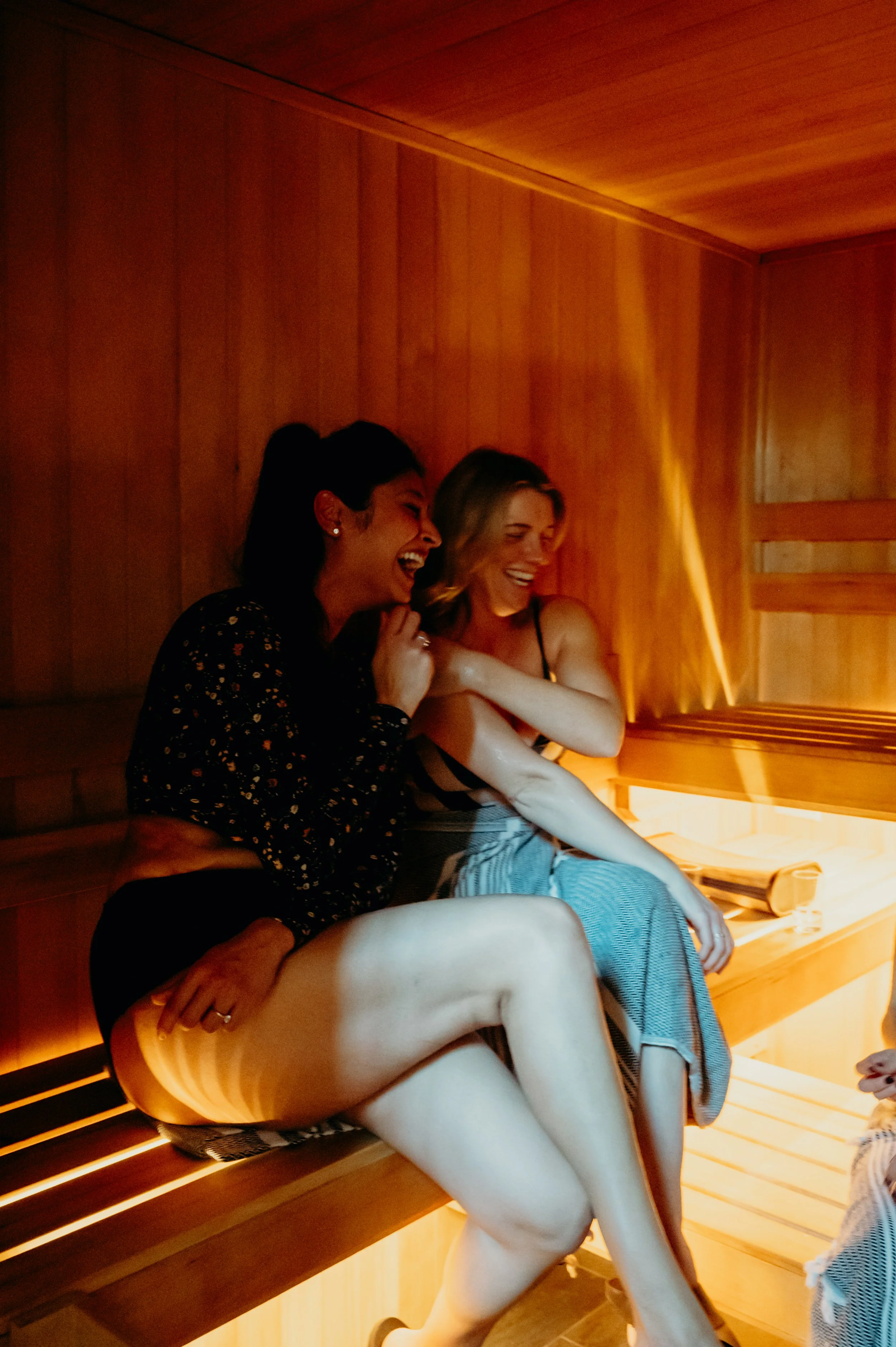 Two women laughing and enjoying themselves inside a wooden sauna.