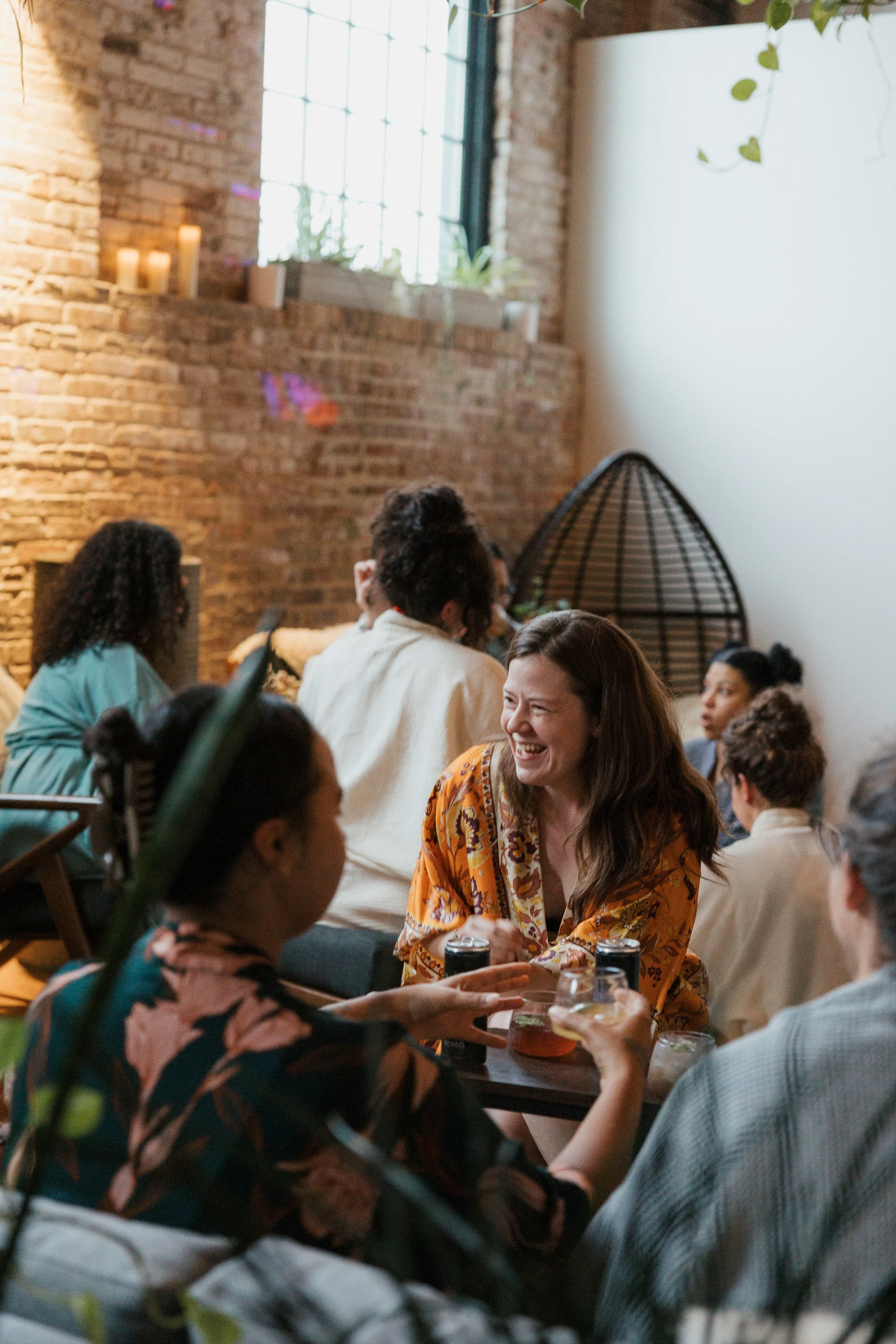 Group of people enjoying drinks and conversation in a cozy indoor space with exposed brick walls.