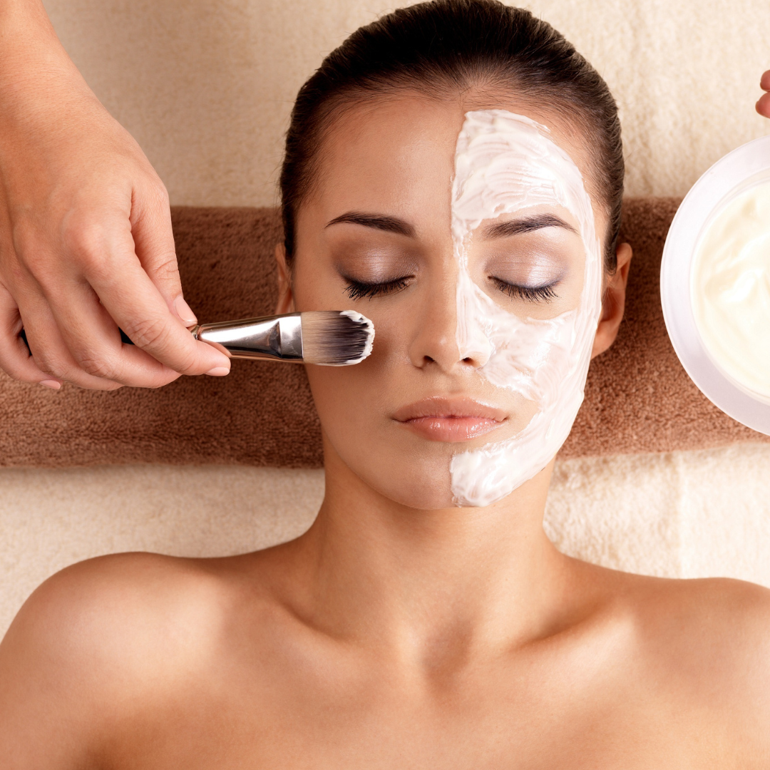 A woman receives a facial treatment with a spa mask being applied to her face while lying down with her eyes closed.