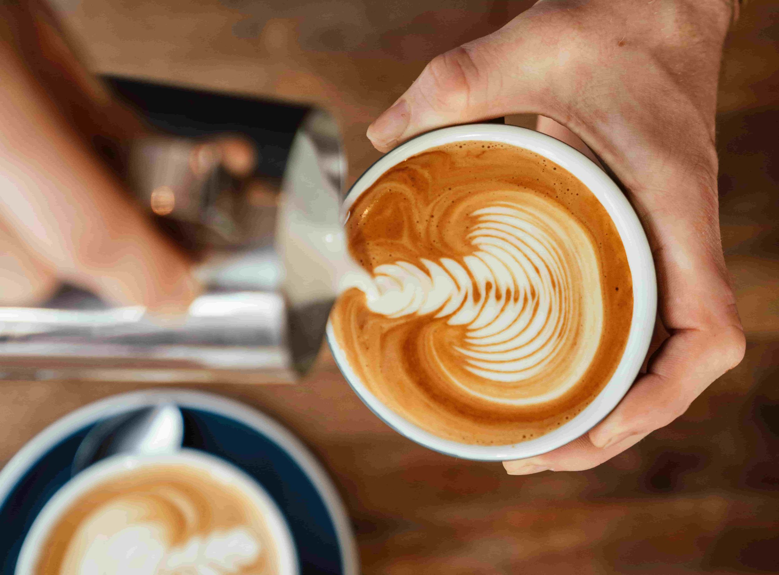 Person pouring steamed milk into a cup of espresso to make latte art.