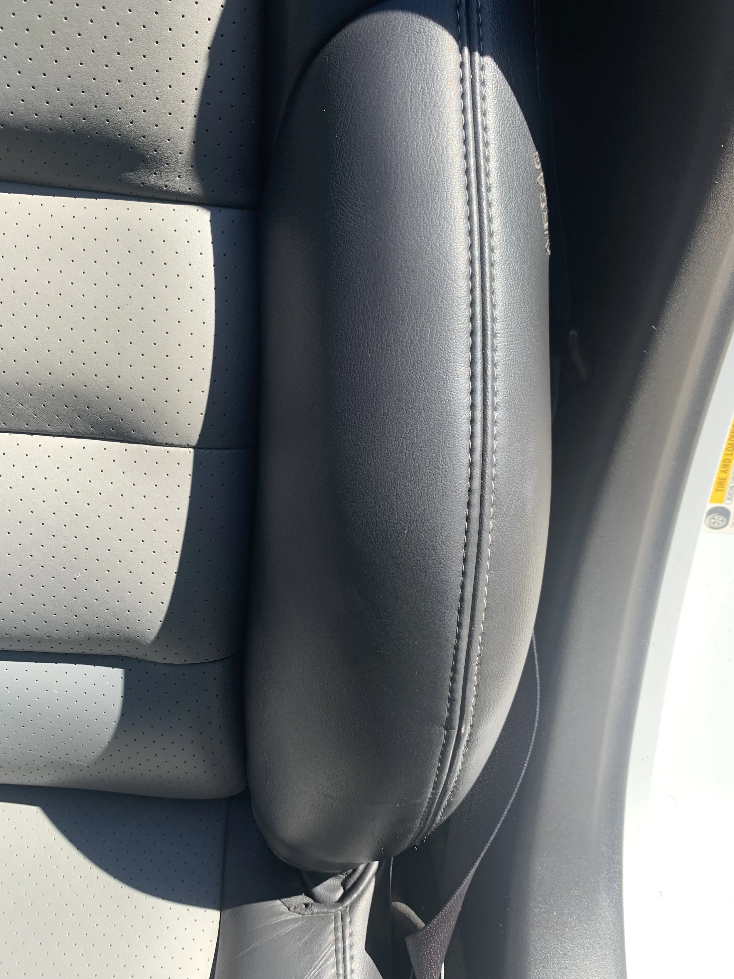 Close-up of a car seat with perforated light gray leather and a black leather headrest with Double Stitch seam.