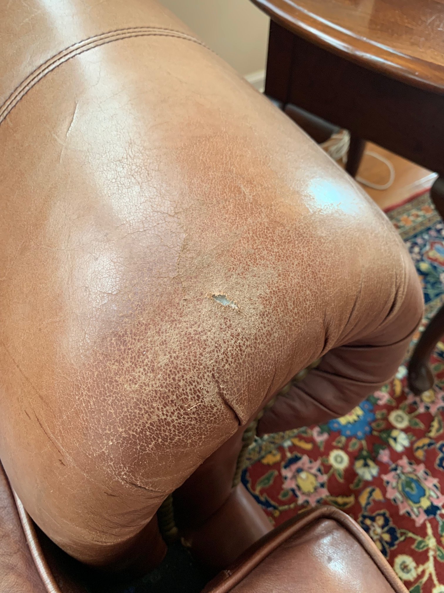 Close-up of a worn, cracked, light brown leather armrest on a vintage armchair.