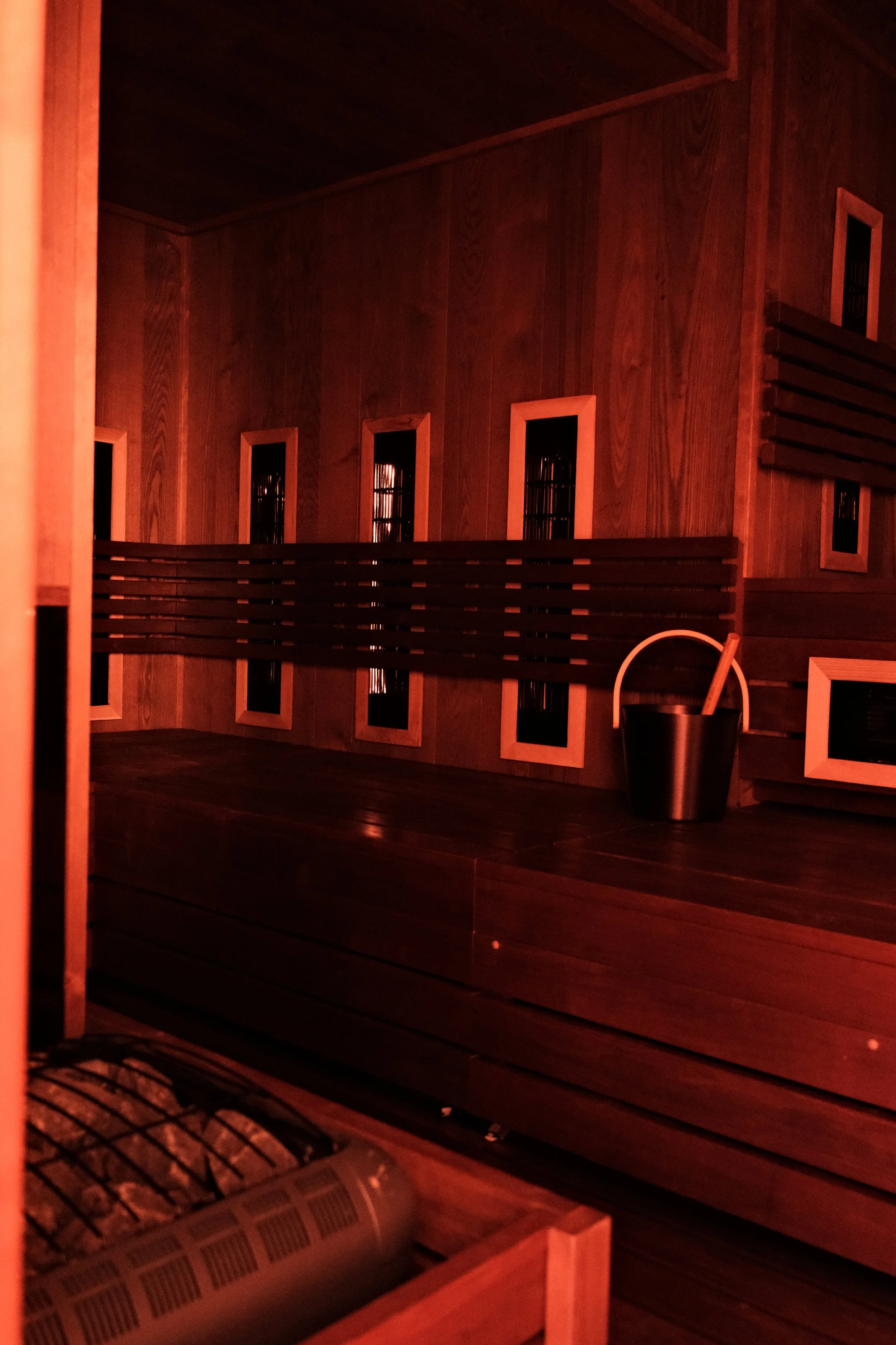 Interior of a sauna with wooden benches and walls, and orange-tinted infrared heating panels.