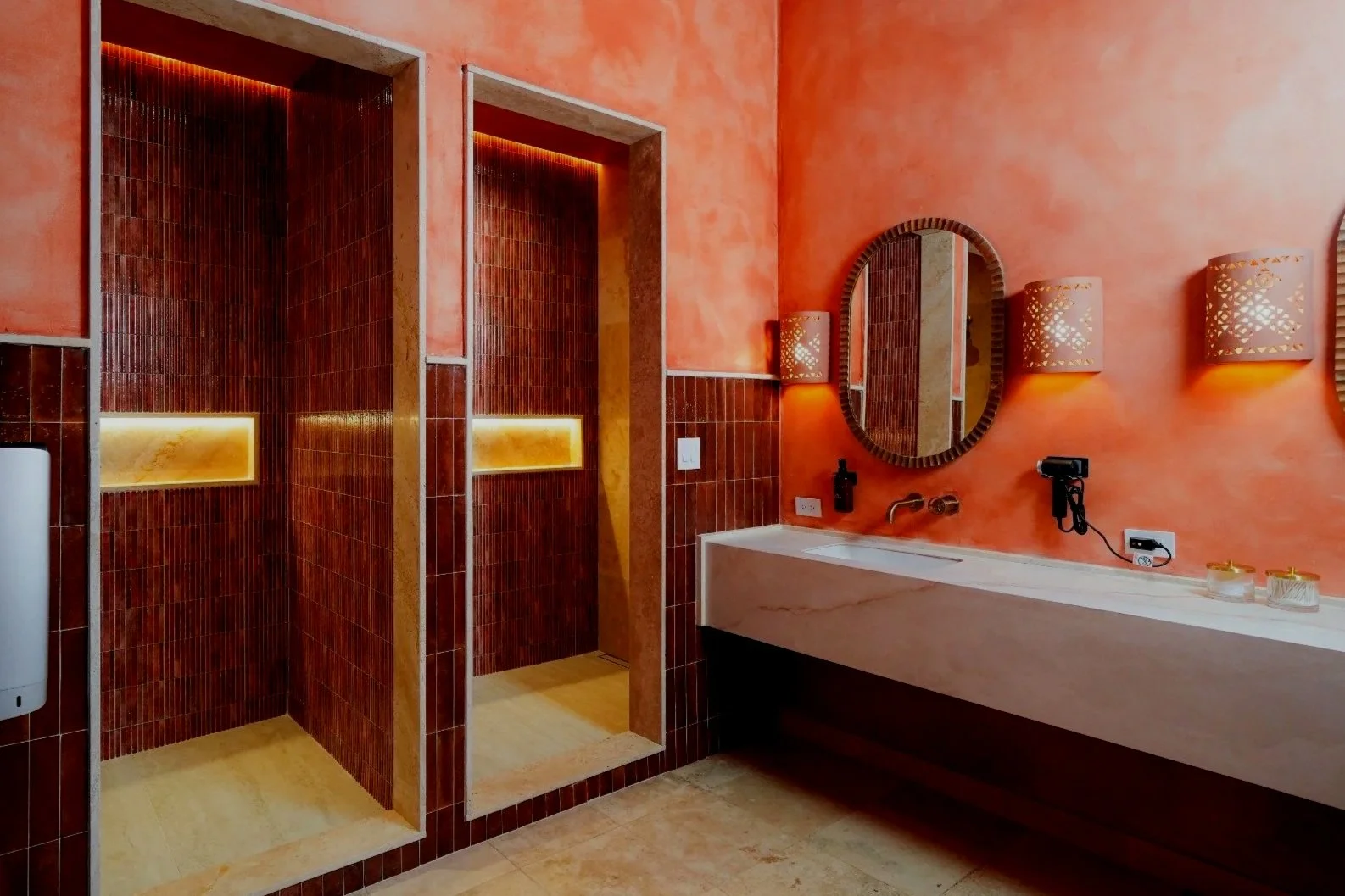 A small bathroom with reddish-brown textured wall tiles, a white modern toilet, a beige floor, and brown grab bars on the wall.