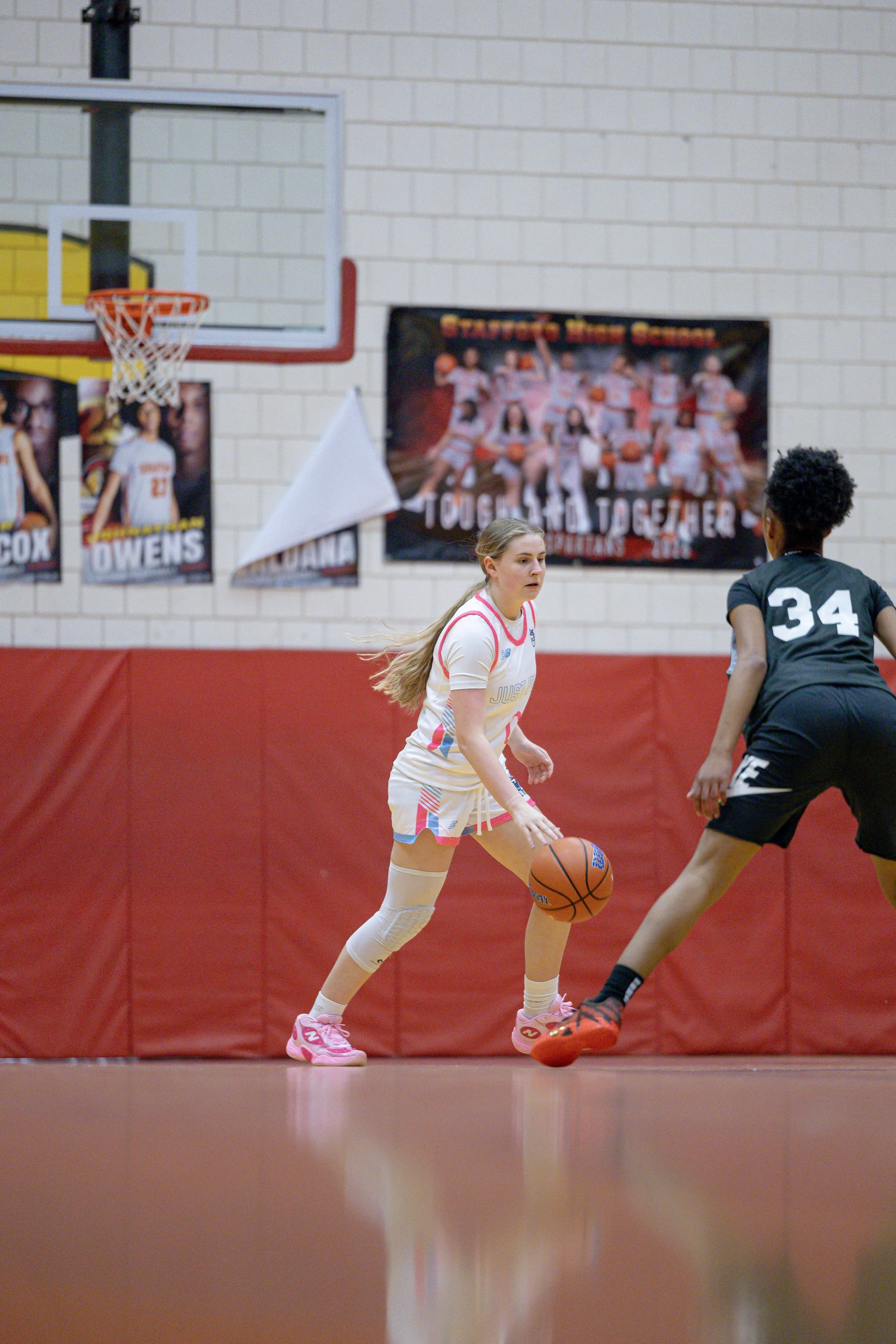 A female basketball player dressed in a white, blue, and black uniform with the phrase "JUST PLAY" and the number 1, standing on an indoor basketball court.
