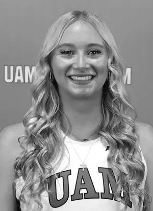 A young woman with braids smiling at the camera, wearing a basketball jersey with the number 12 and the words 'Made Creek,' along with layered necklaces.