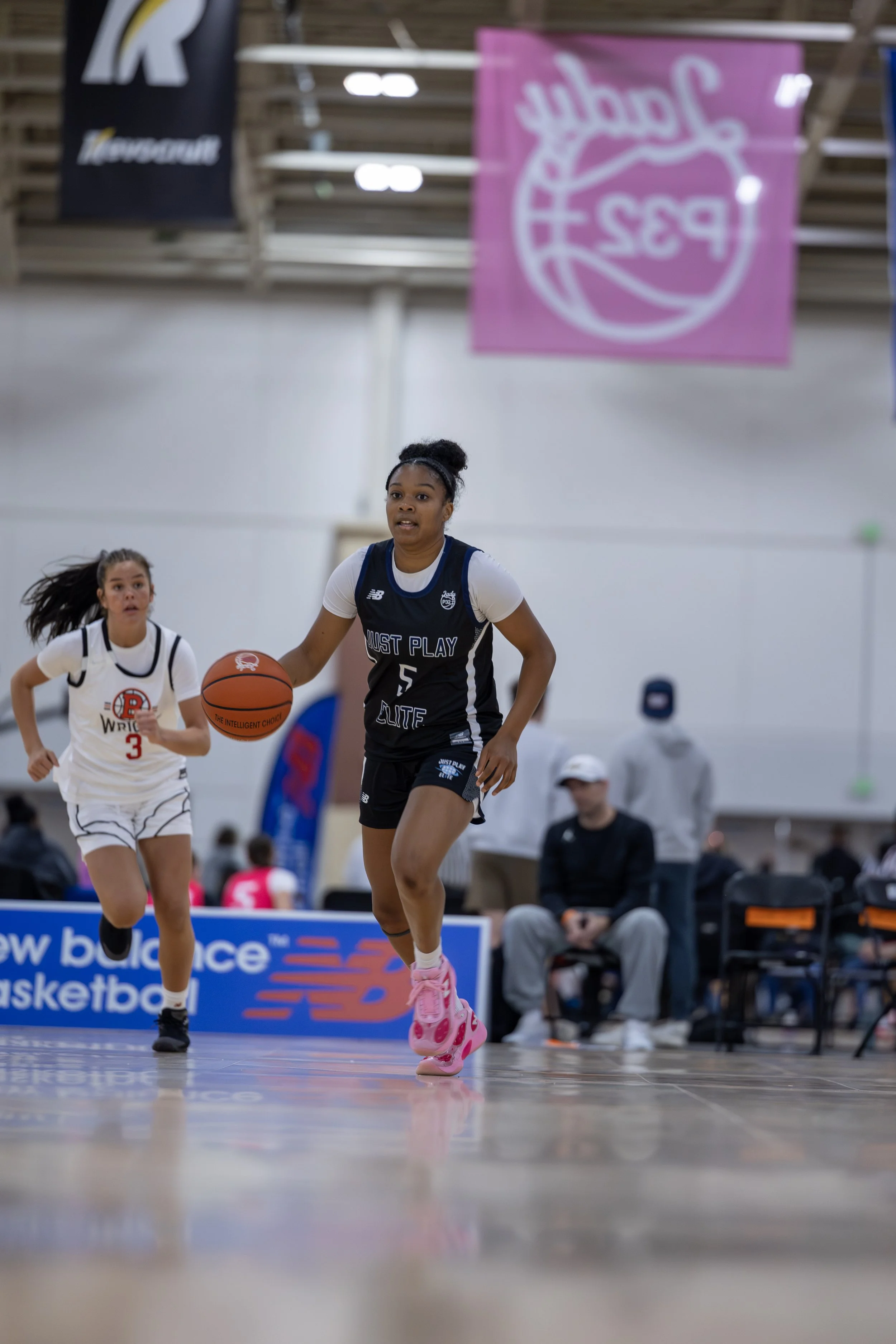 A female basketball player dressed in a white, blue, and black uniform with the phrase "JUST PLAY" and the number 1, standing on an indoor basketball court.
