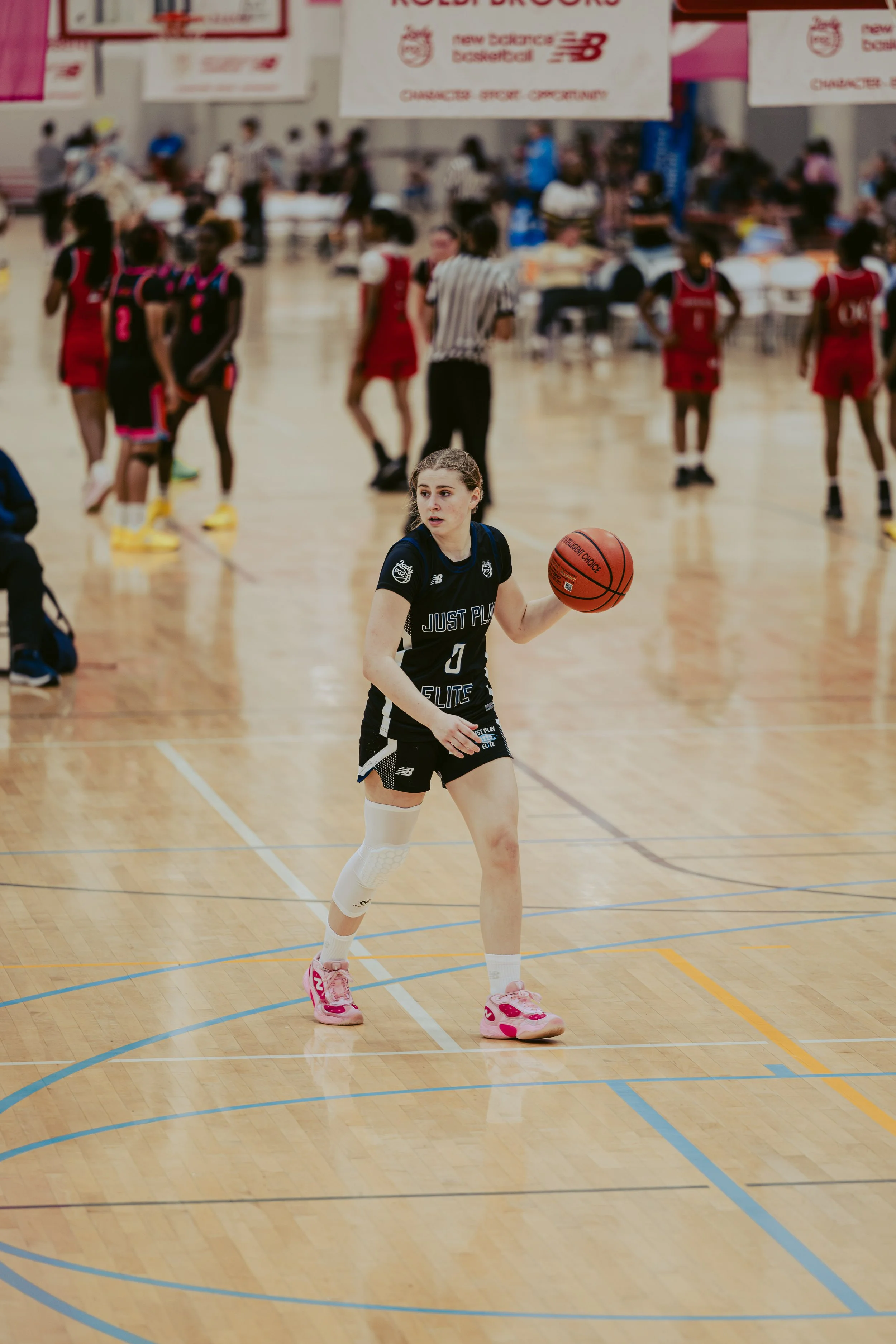 A female basketball player with long blonde hair in braids, wearing a blue and white uniform, prepares to jump for a rebound on an indoor basketball court.