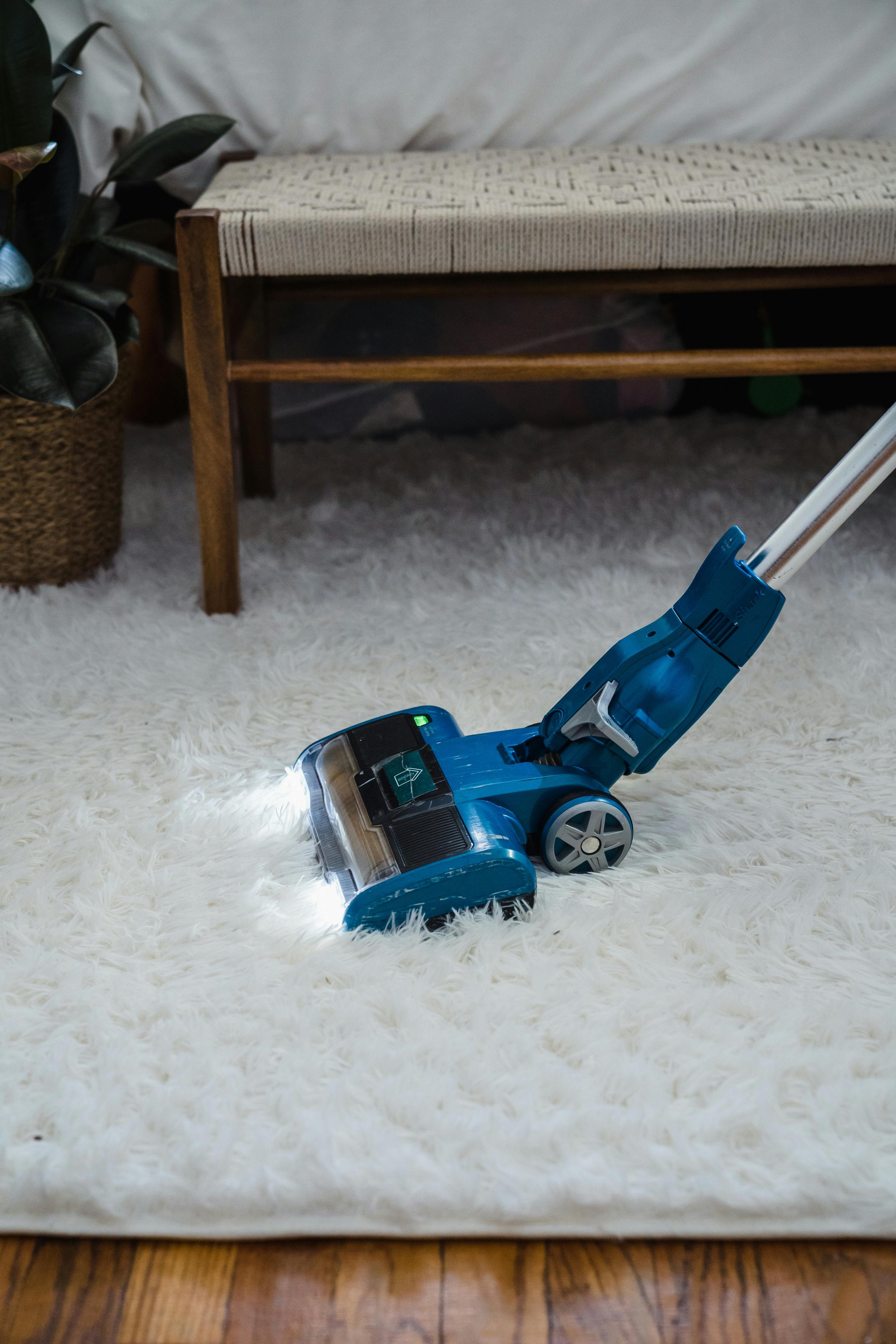 A modern cordless stick vacuum cleaner cleaning a white shag rug in a living room.