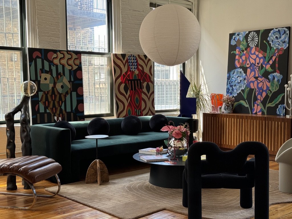 Eclectic living room with abstract art, dark green sofa, modern chairs, and round paper lantern.