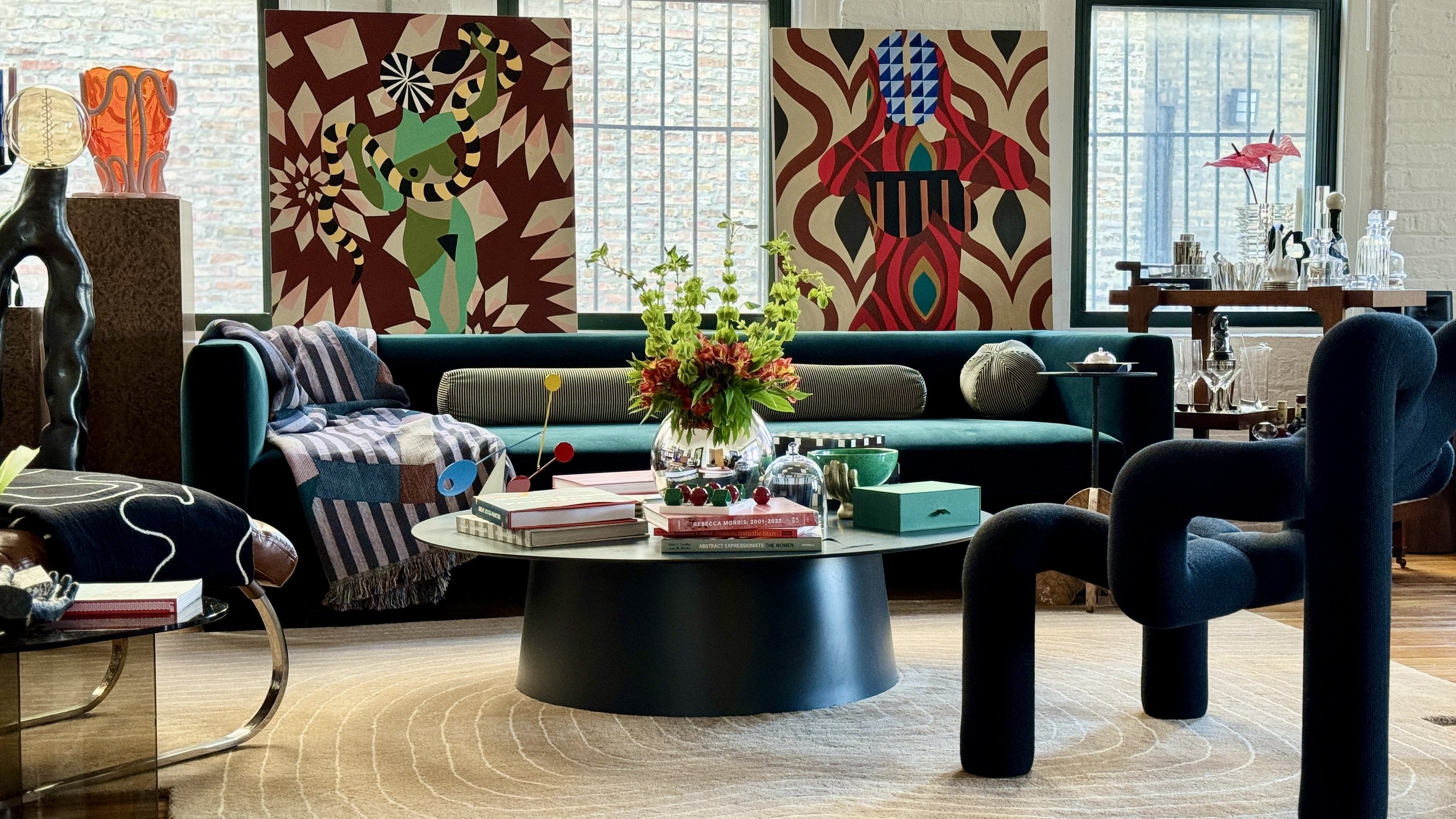 Stylish living room with abstract art, modern furniture, green couch, round coffee table with plants, books, and colorful decor.