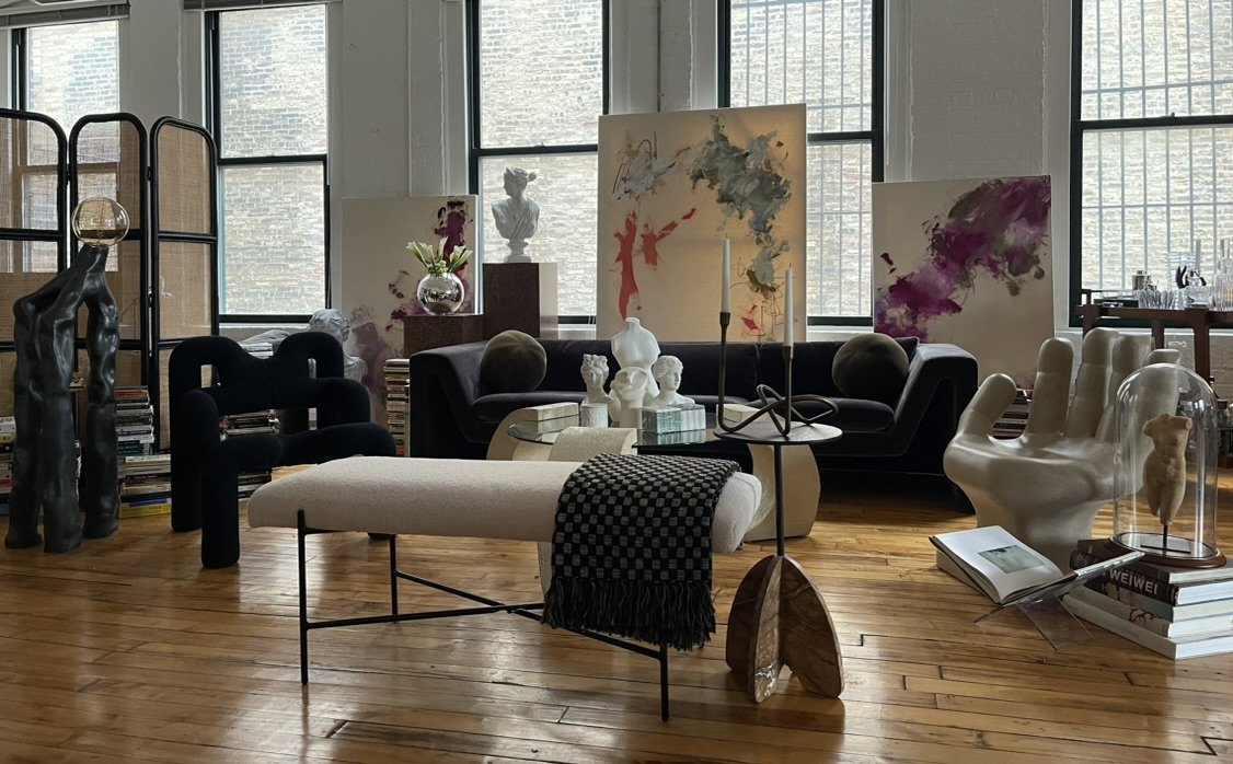 Stylish modern living room with eclectic decor, featuring abstract art, unique sculptures, and contemporary furniture against a backdrop of large windows.