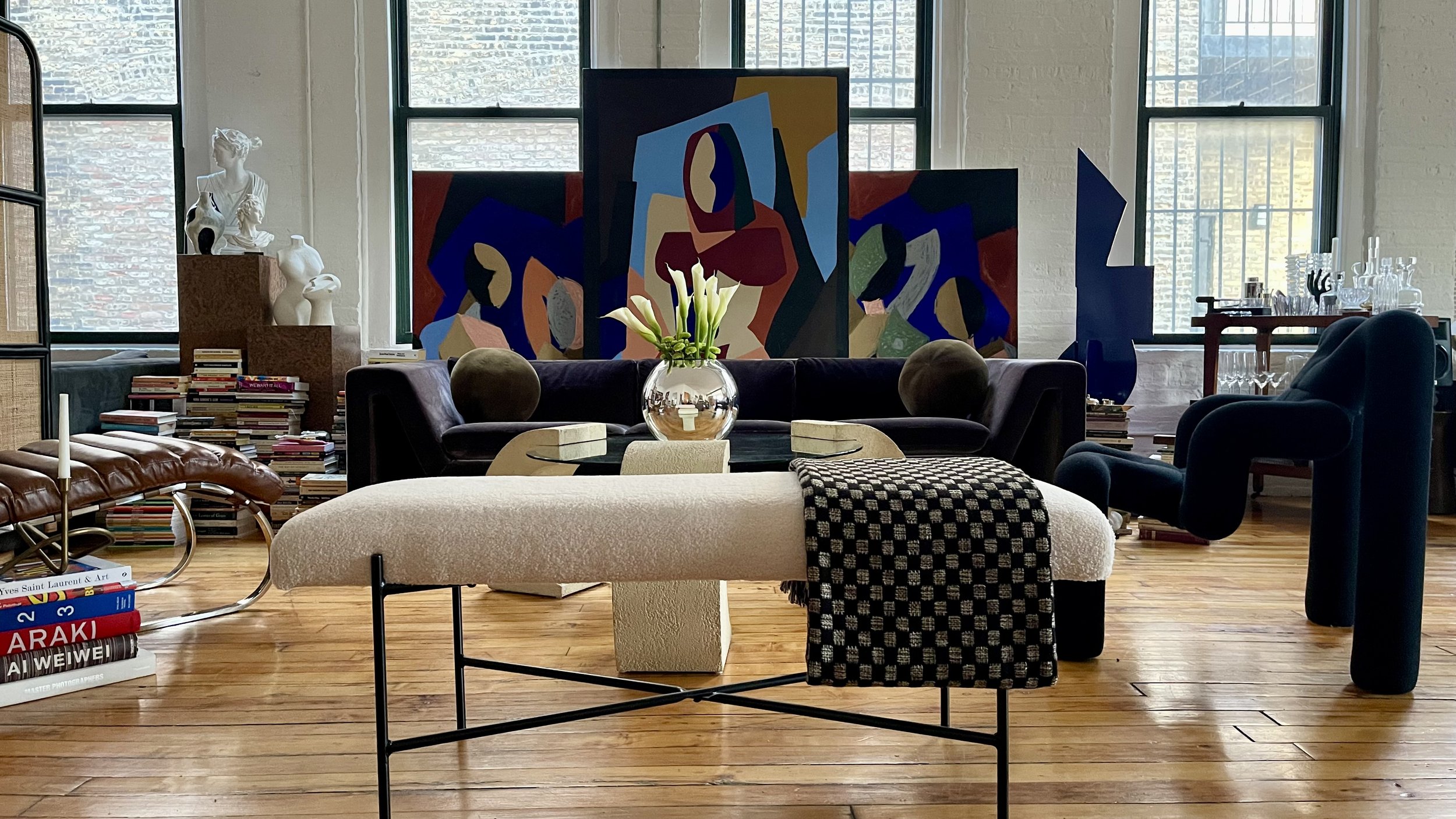 Stylish living room with art, sculptures, a bench, and velvet furniture.
