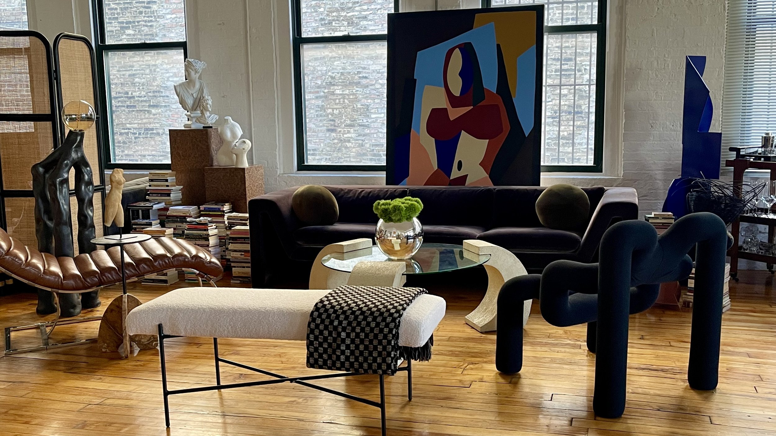 Stylish living room interior with modern furniture, abstract art, sculptures, books, and a large painting of a geometric figure.