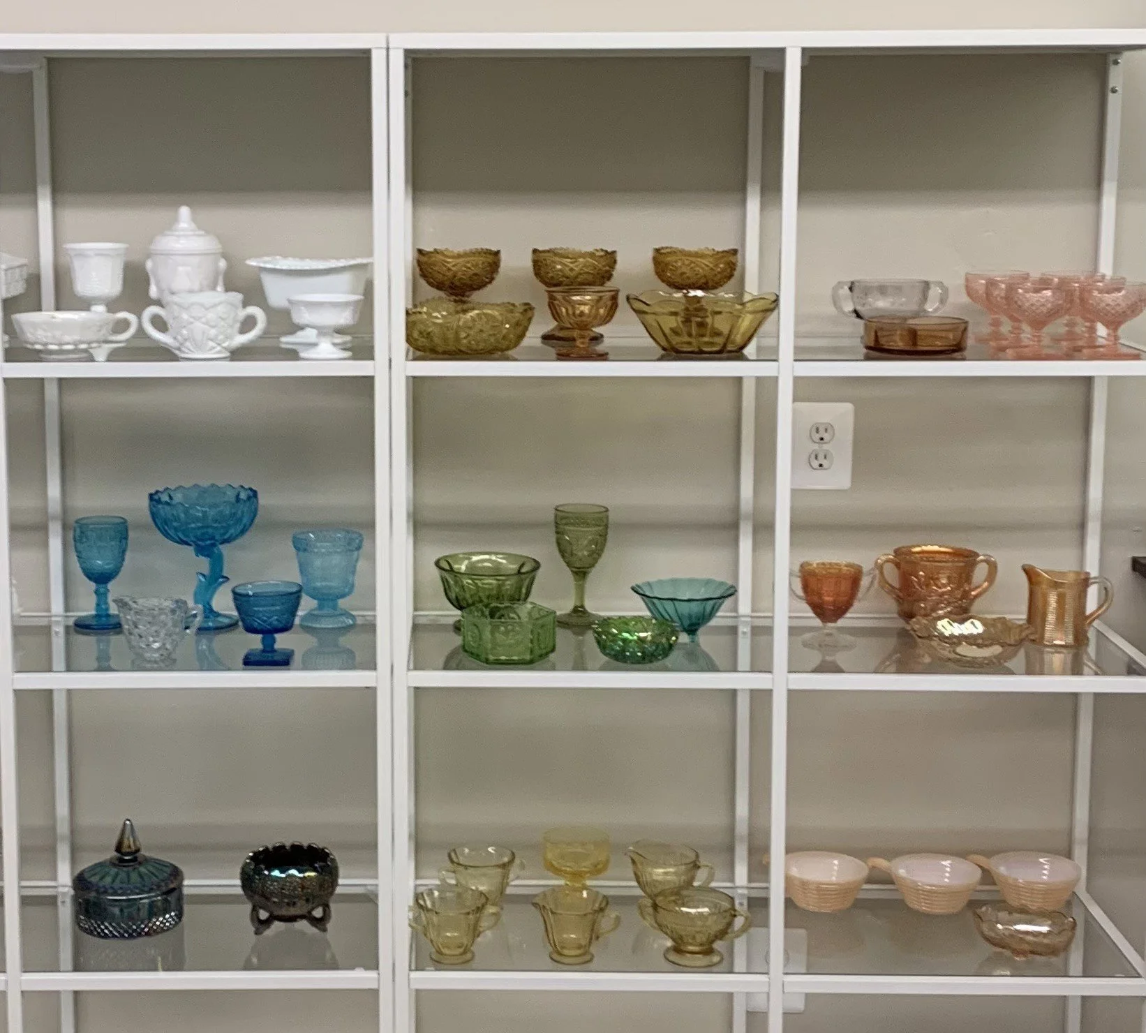 Colorful glassware collection displayed on shelves, including bowls, cups, and dishes in various colors such as blue, green, amber, and pink.