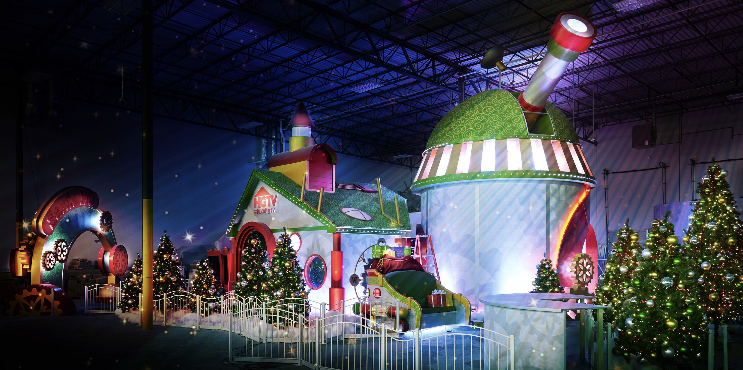 Indoor holiday display with decorated Christmas trees, whimsical toy houses, and colorful props, illuminated with bright lights.