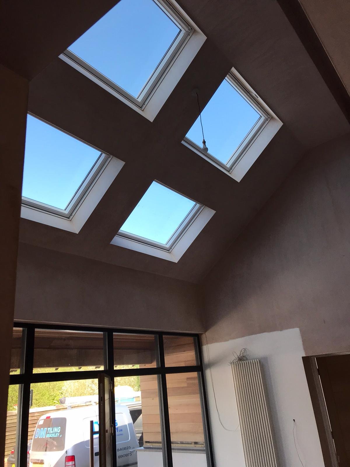 Interior view of a room with four large rectangular skylights on the sloped ceiling showing a clear blue sky, a white radiator on the wall, and a sliding glass door leading outside.