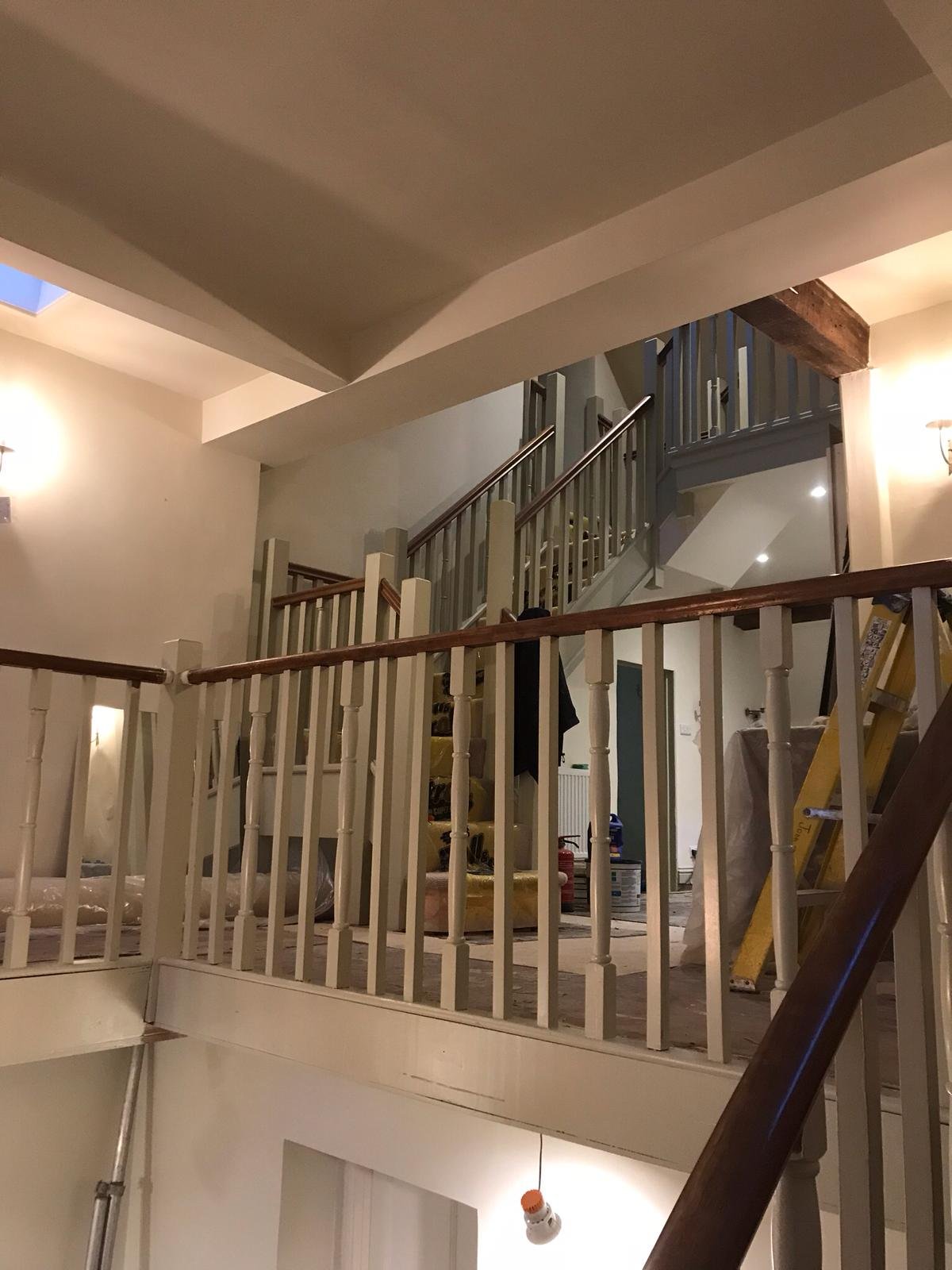 Interior of a home with a staircase, railing, and construction or renovation supplies visible, including a yellow ladder and buckets.