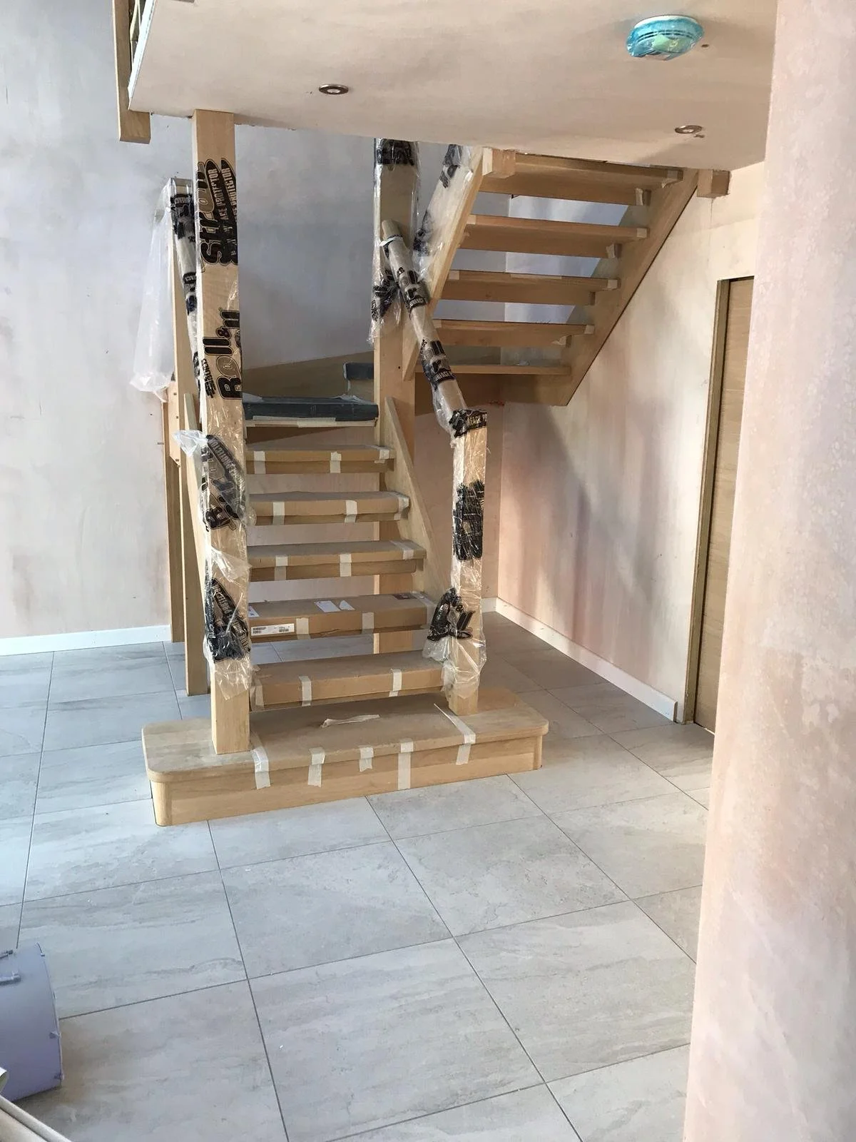 Unfinished wooden staircase in a room under construction, with protective plastic wrap on some parts.