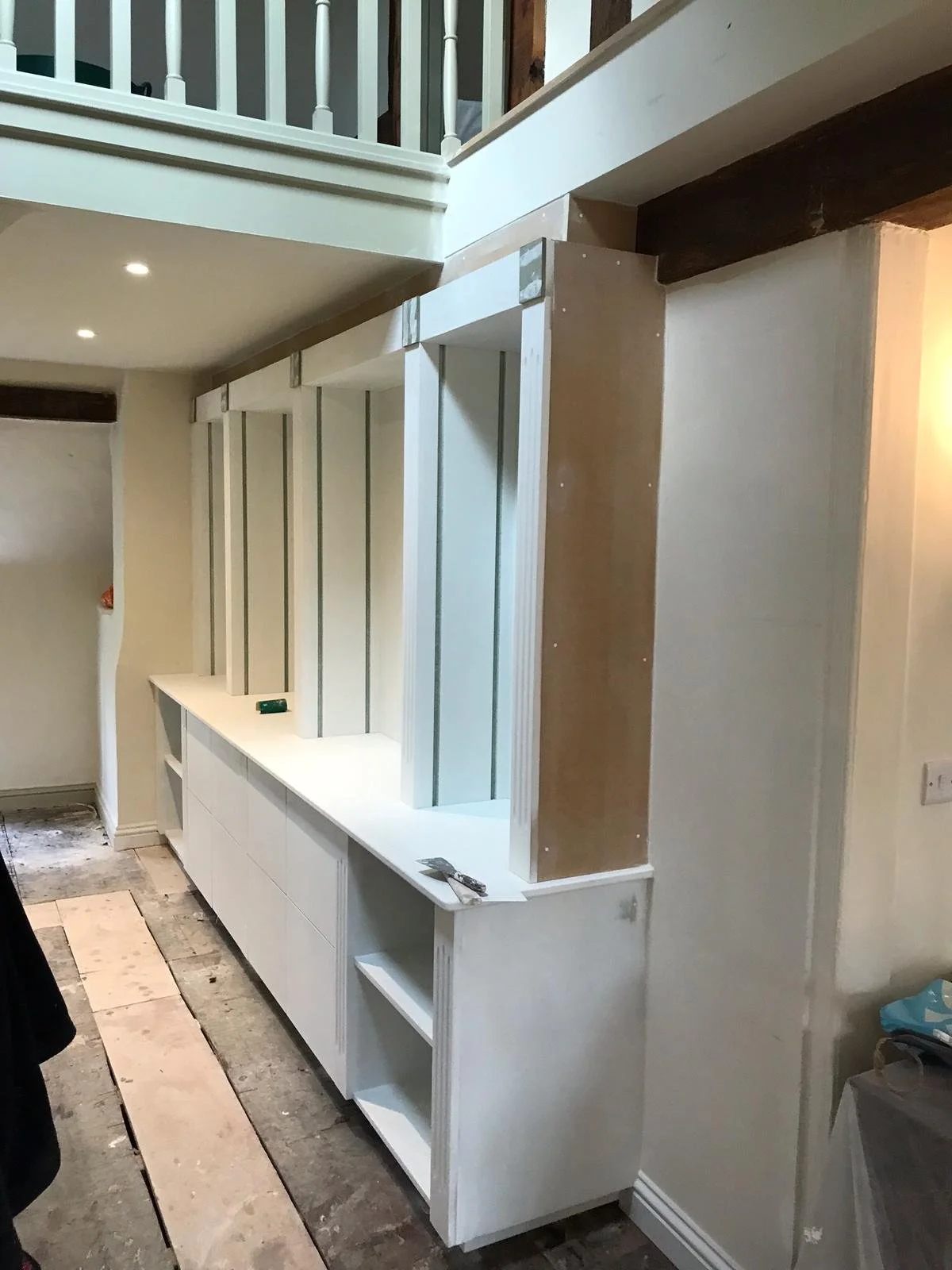 Interior view of a doorway under construction with white cabinetry and exposed wood framing, with stairs and a railing above.