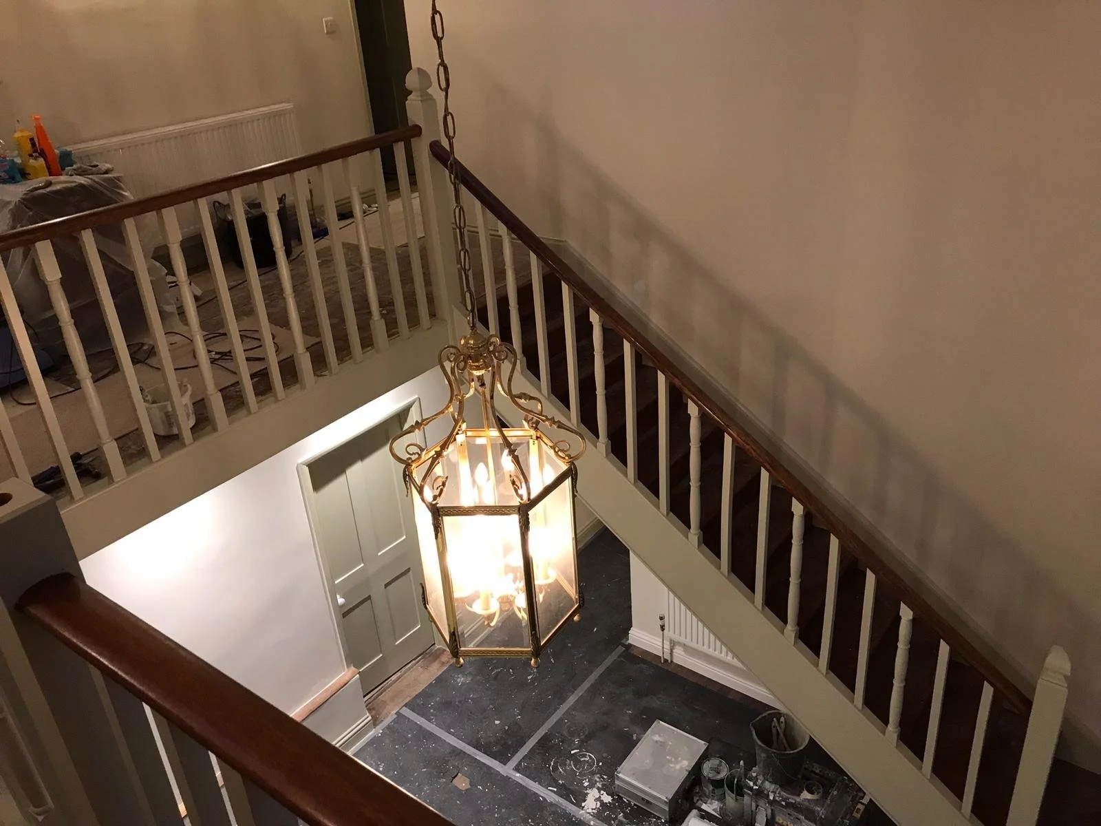 Overhead view of a hallway with a chandelier, staircase railing, and a partially visible room with stairs, construction tools, and supplies.