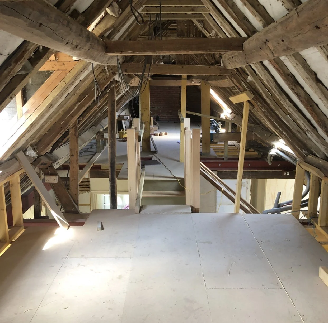 Attic space under construction with exposed wooden beams, framing, and insulation in the process of being installed.