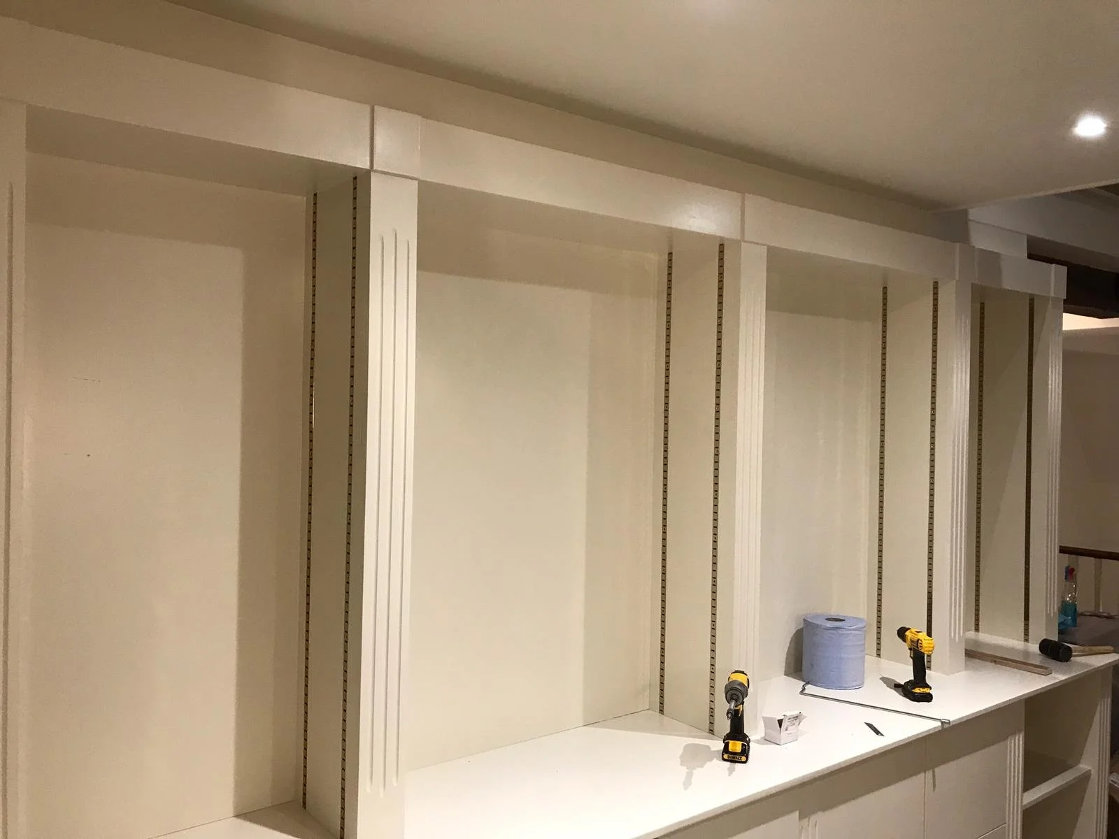 Inside view of a partially assembled built-in cabinet with vertical sections, tools, and tape on a white countertop.
