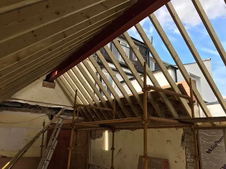Construction site showing a wooden roof framework and scaffolding inside a building under renovation.