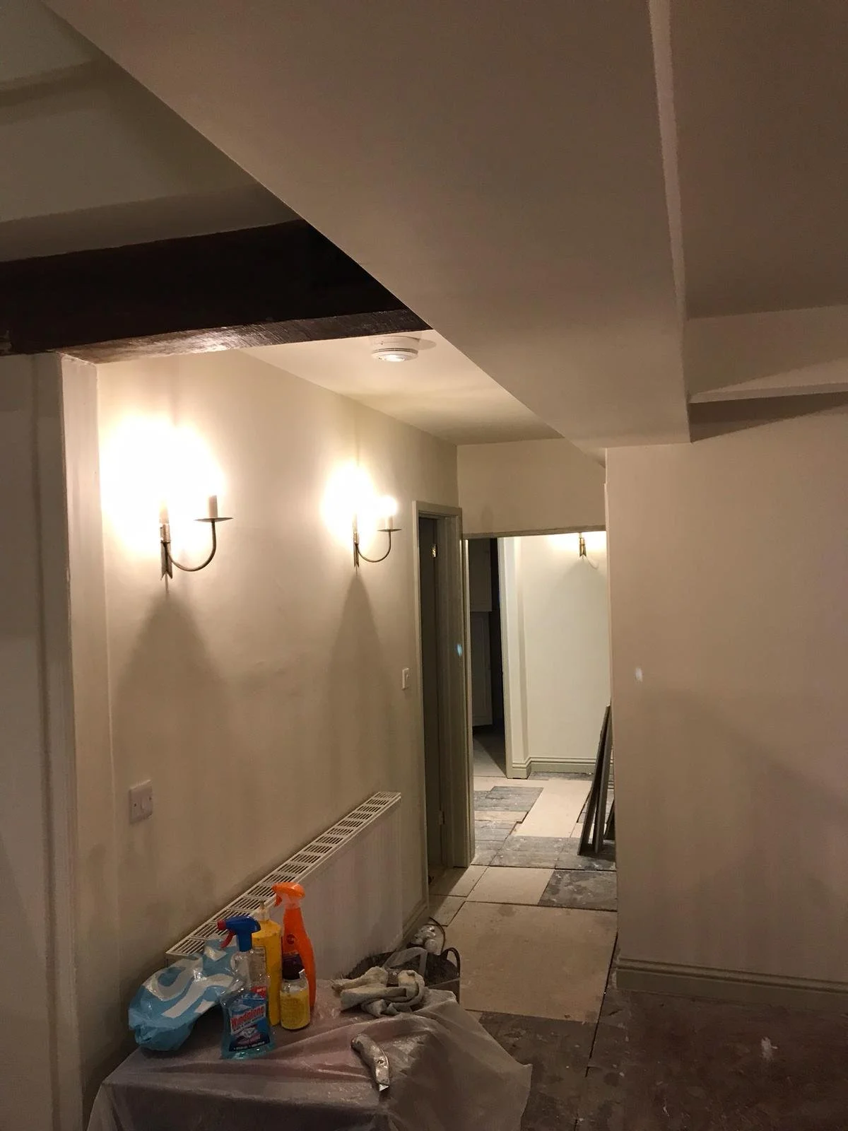 Indoor hallway with construction supplies, wall sconces, and partially finished flooring.