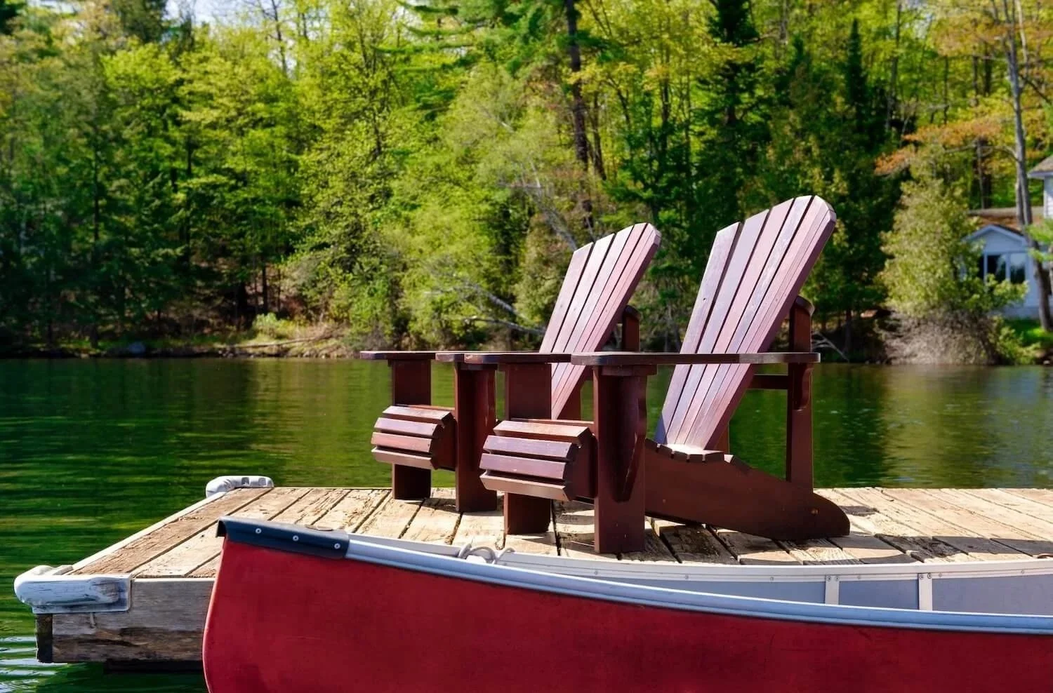 Chairs on a dock next to a red canoe in the water on a Sutton, MA lake.