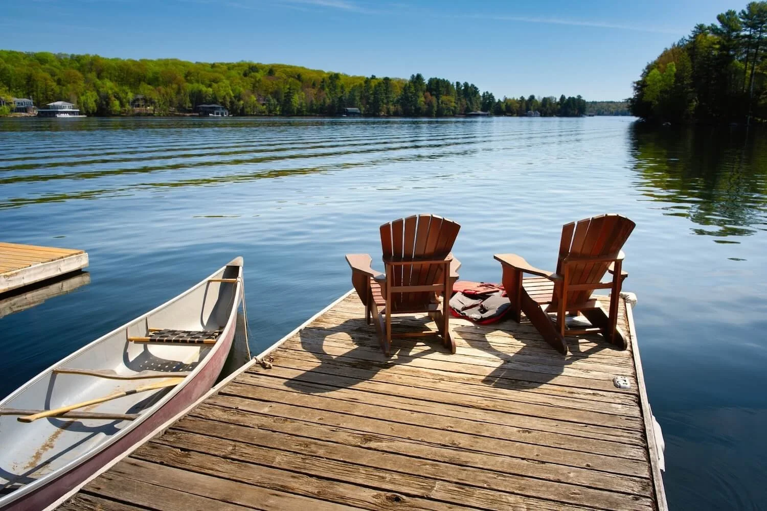 A wooden dock on a lake in Westborough, MA with two Adirondack chairs facing the water.