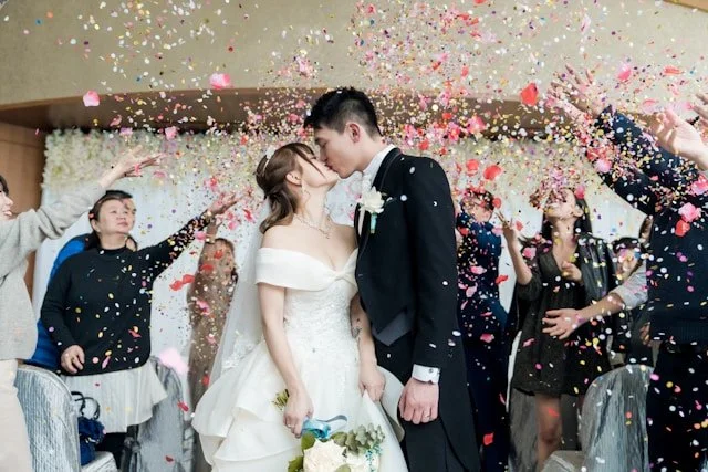 A bride and groom kissing as guests throw confetti at a wedding celebration.