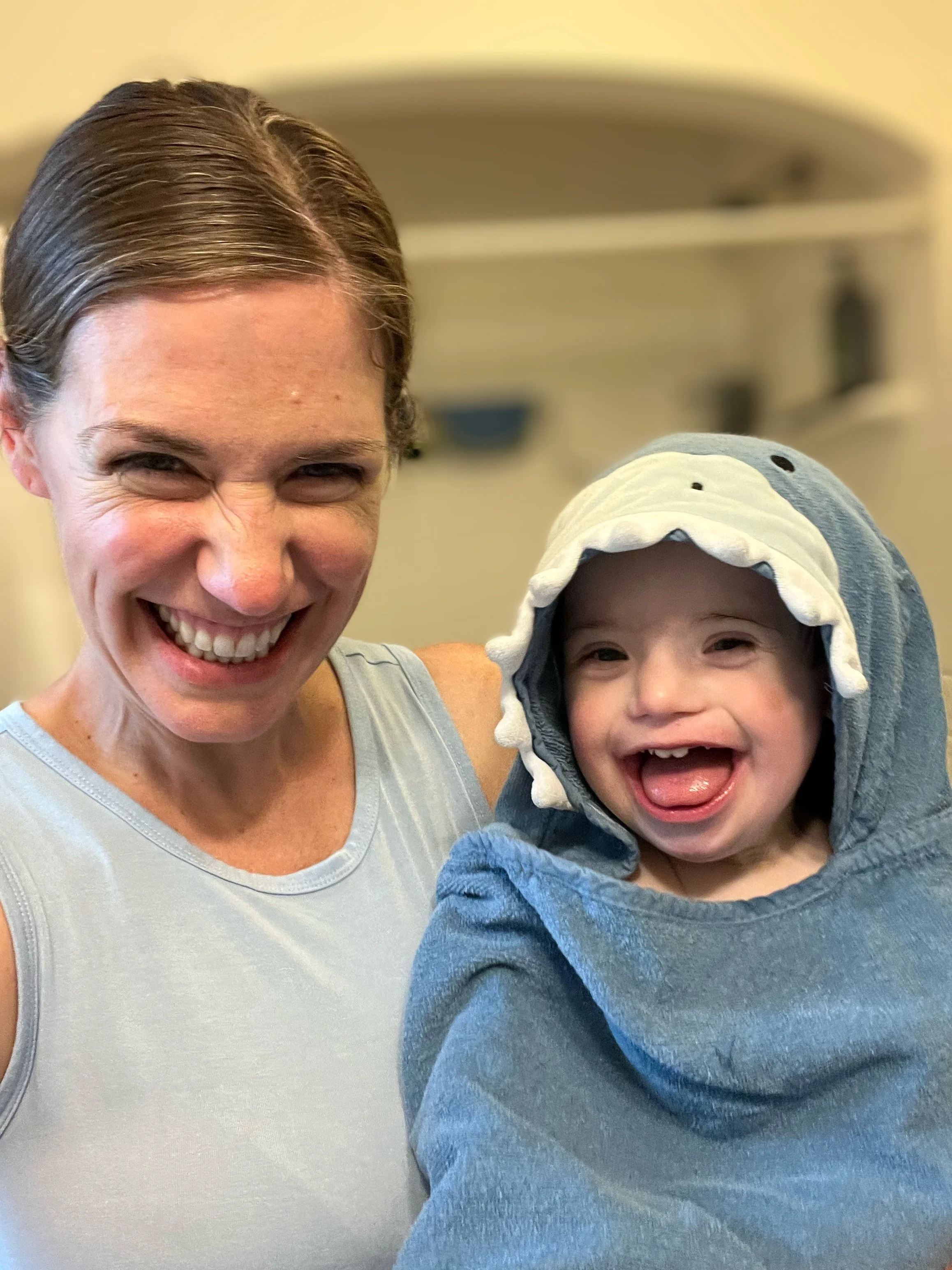 A woman smiling and holding a young child dressed in a shark hoodie, both showing happy, laughing expressions.