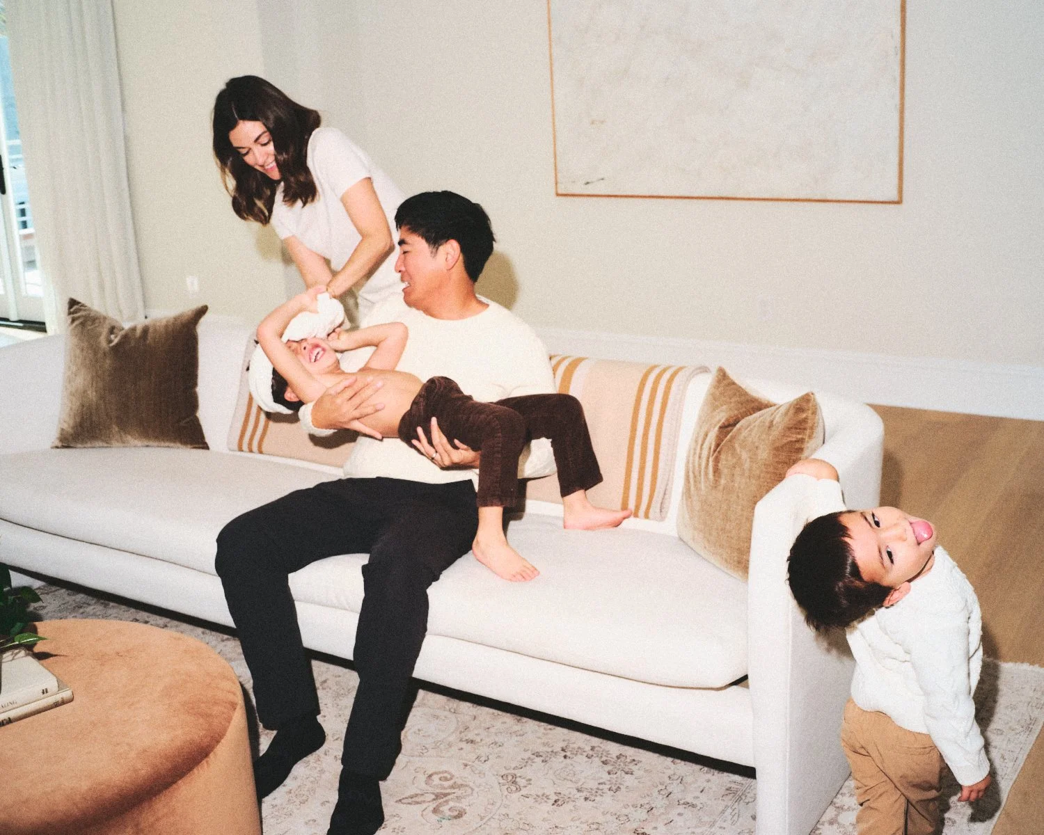 Documentary flash photography of a family of four having fun on a white sofa in a living room in NYC, with a woman, a man, and two children playing and relaxing being photographed by Madivan Studios.
