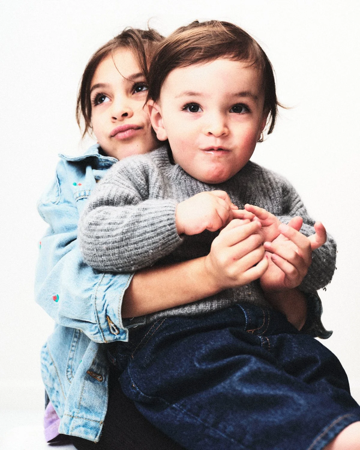 Two young children, a girl and a boy, are playfully posing. The girl is hugging the boy from behind, and both have playful expressions on their faces. Photographed in monochrome by Madivan Studios in New York City.