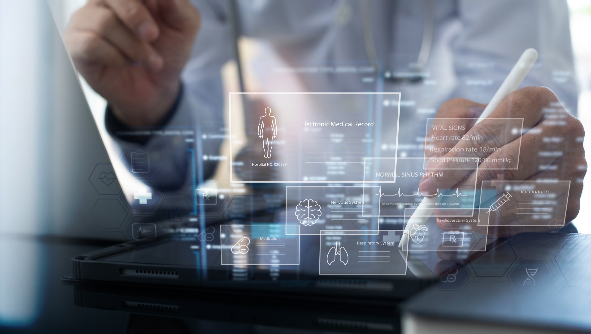 A person using a stylus on a tablet with holographic digital medical interface overlays showing health data and medical icons.