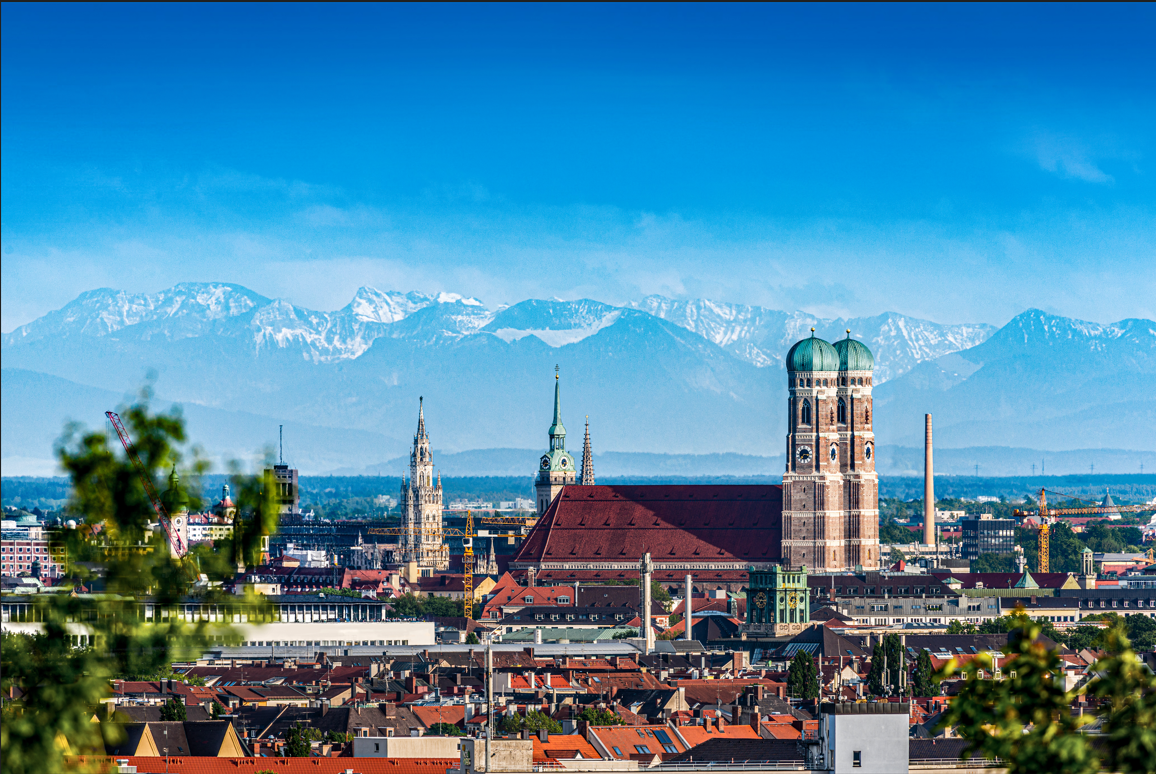 City skyline with historic church towers and mountains in the background.