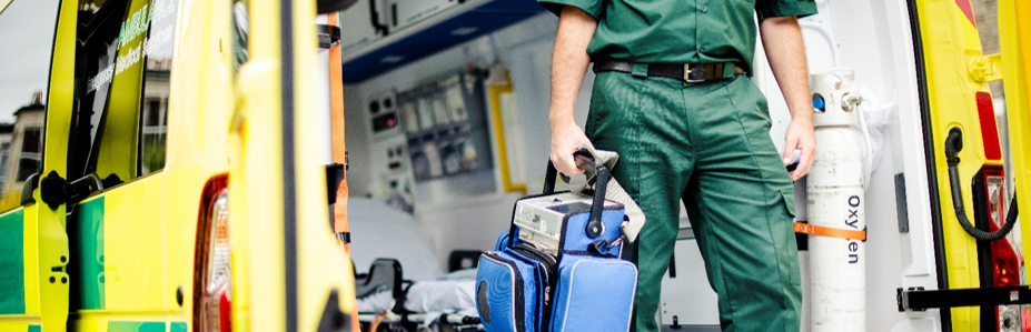 Emergency medical technician dressed in green uniform holding medical equipment bag inside an ambulance.