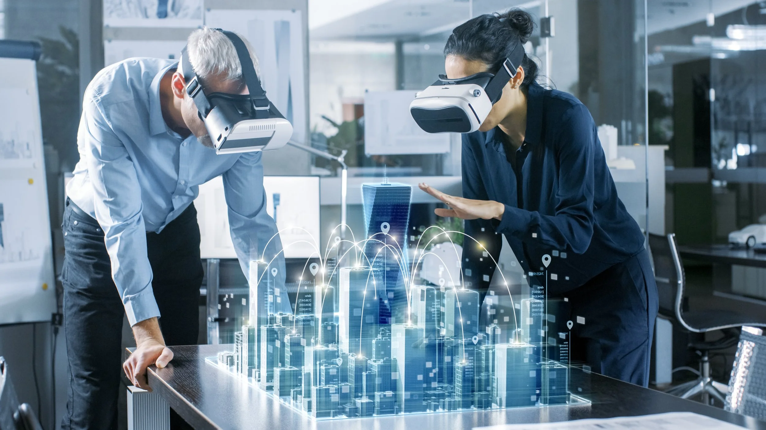 Two people wearing virtual reality headsets and interacting with a holographic city model on a table in a modern office.